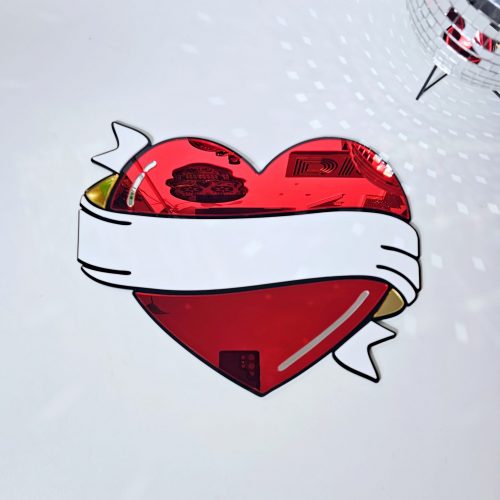 A handmade mirror in the style of a traditional tattoo heart with banner through the middle. The heartis red with a black outline and white banner with silver and gold mirror accents.