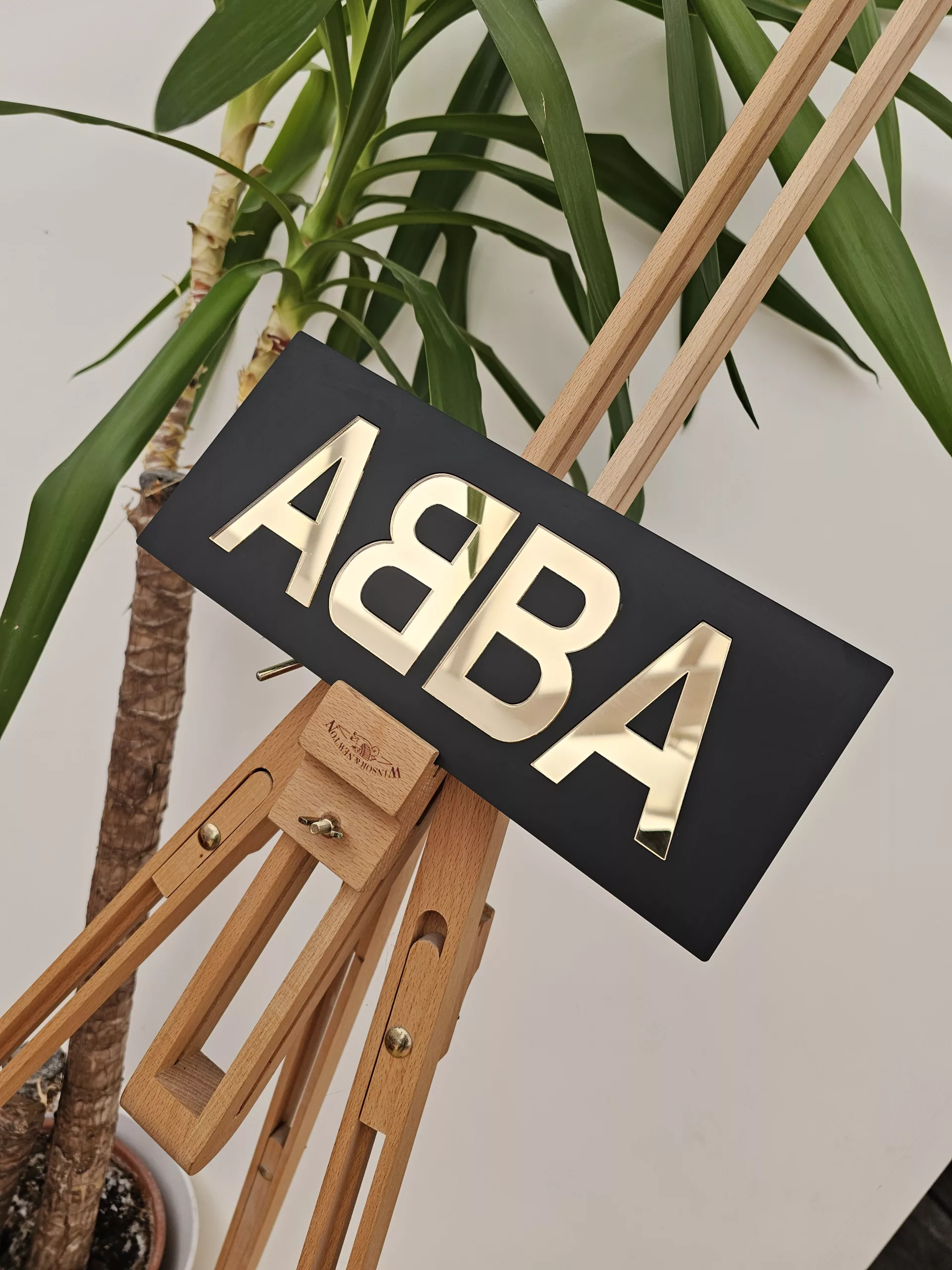 A piece of handmade wall art made with matt black acrylic and the word ABBA in gold mirror lettering.