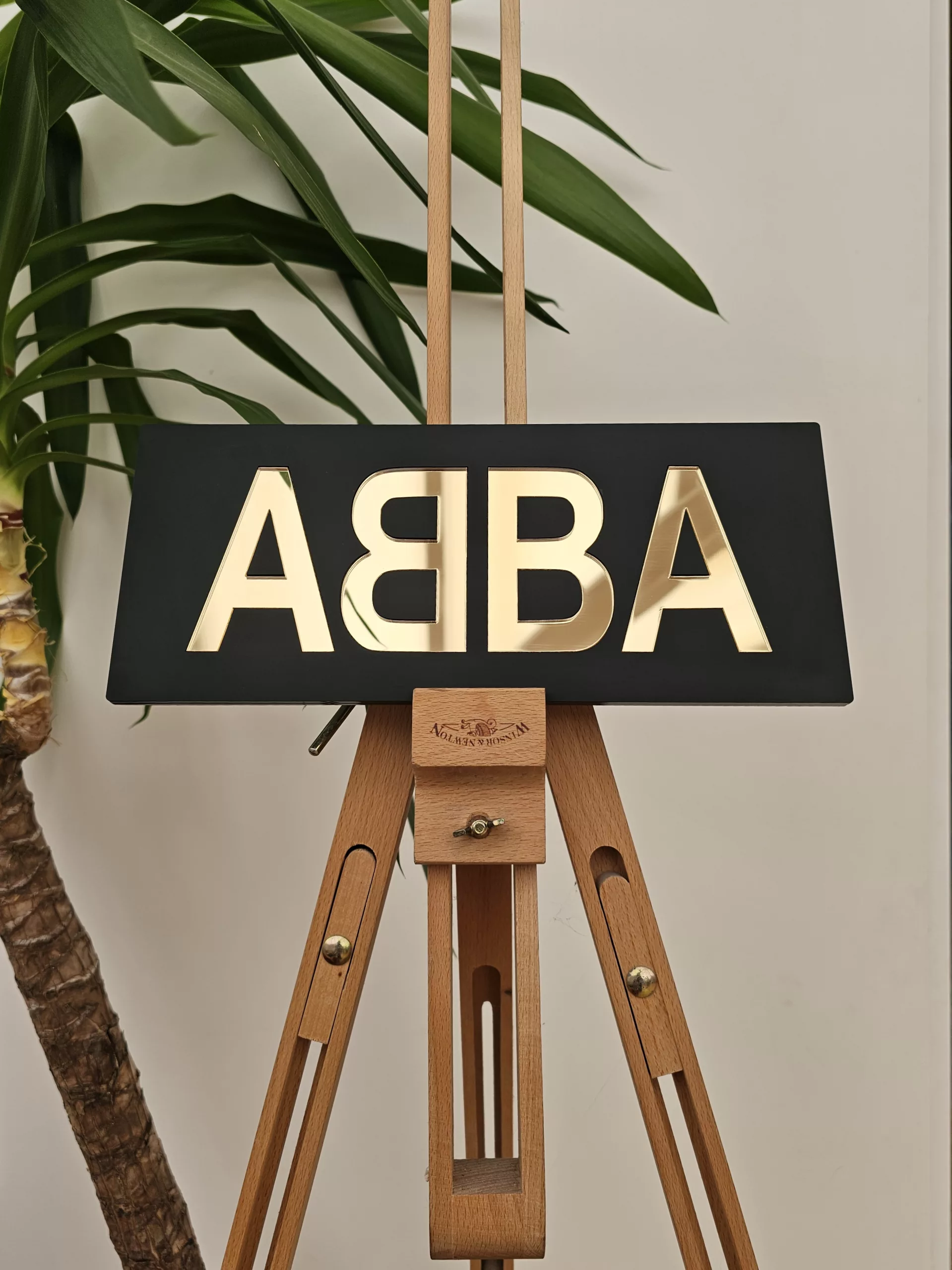 A piece of handmade wall art made with matt black acrylic and the word ABBA in gold mirror lettering.