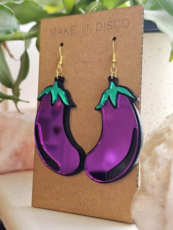 A pair of earrings in the shape of an aubergine. The earrings are purple with a black outline and green details.