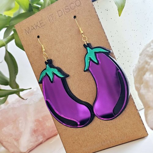A pair of earrings in the shape of an aubergine. The earrings are purple with a black outline and green details.