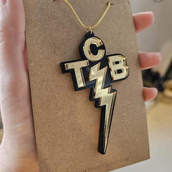A penmdant inspired by the one worn by Elvis Presley. It is black and gold with the letters TCB and a lightning bolt.