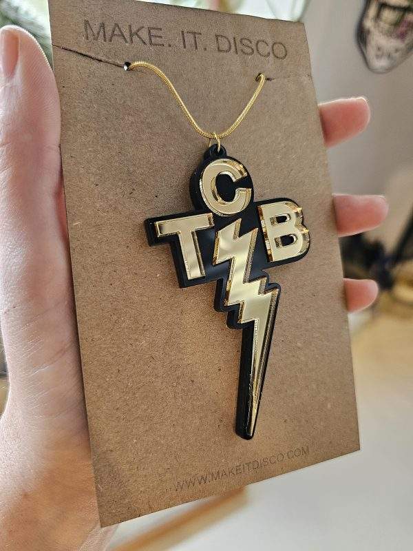 A penmdant inspired by the one worn by Elvis Presley. It is black and gold with the letters TCB and a lightning bolt.