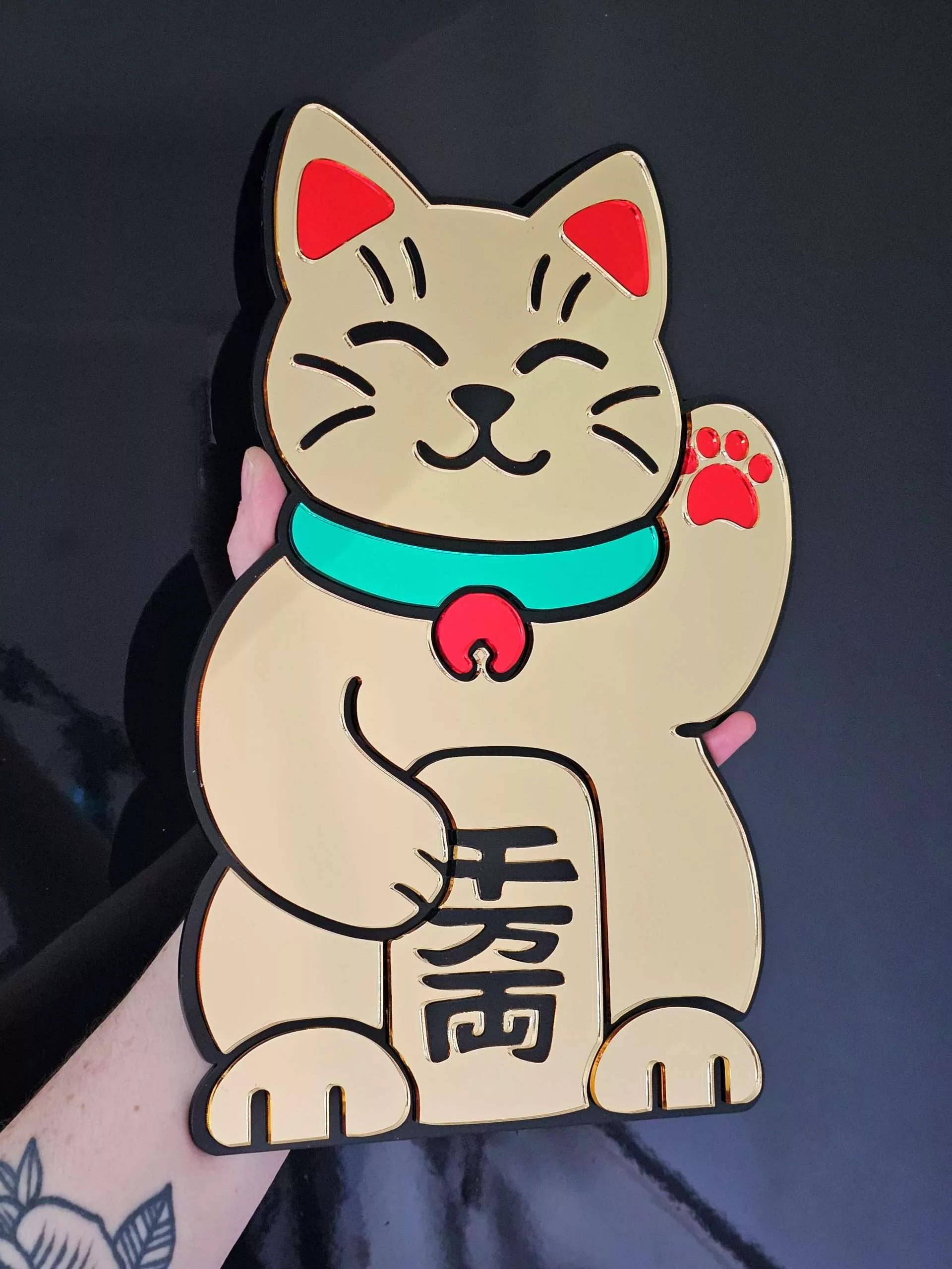 A handmade mirror in the shape of the Japanese waving cat. Made with gold mirror and black, gold and green accents.