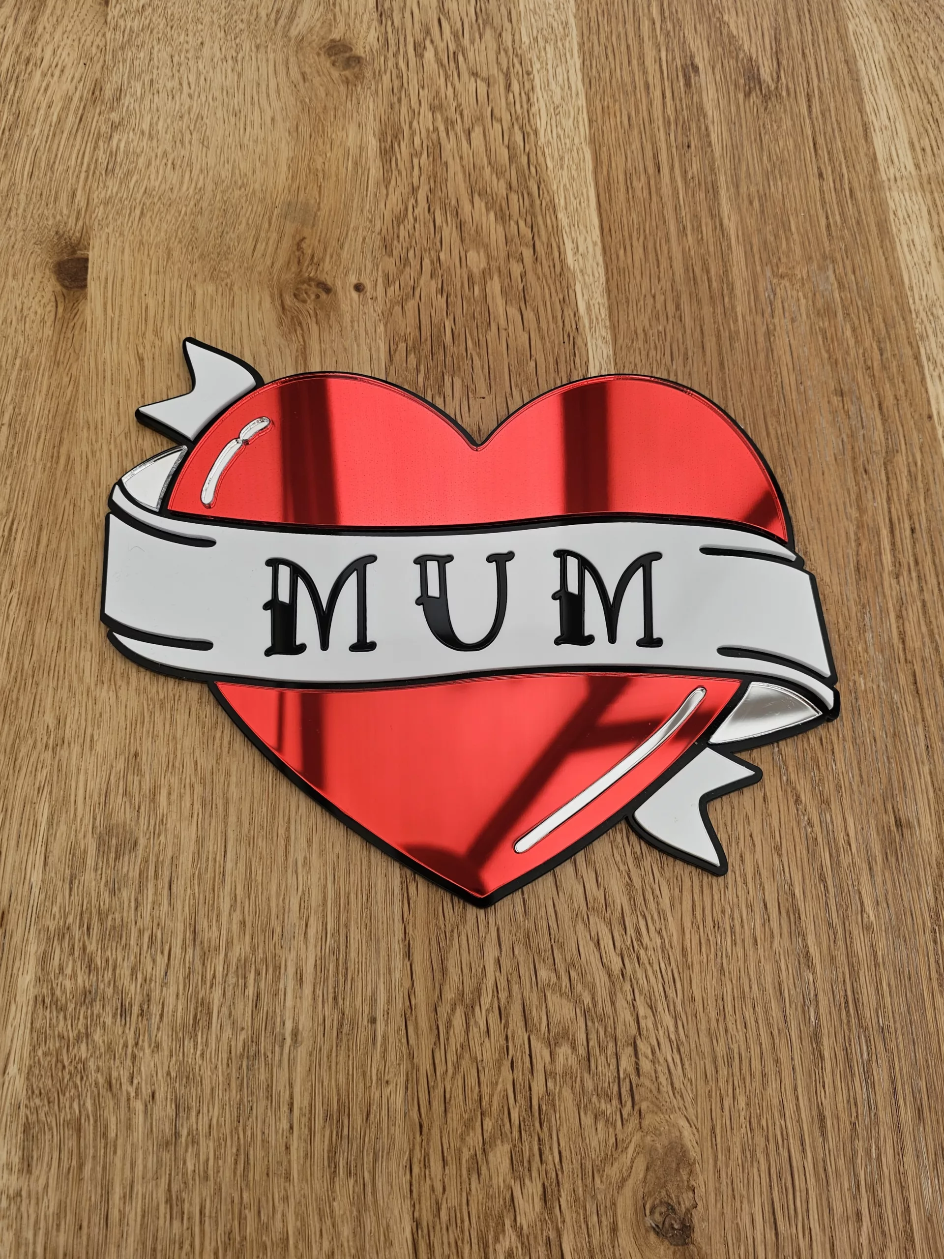 A handmade mirror in the shape of a heart with a banner running through the middle with the word mum. Made in an old school tattoo style.