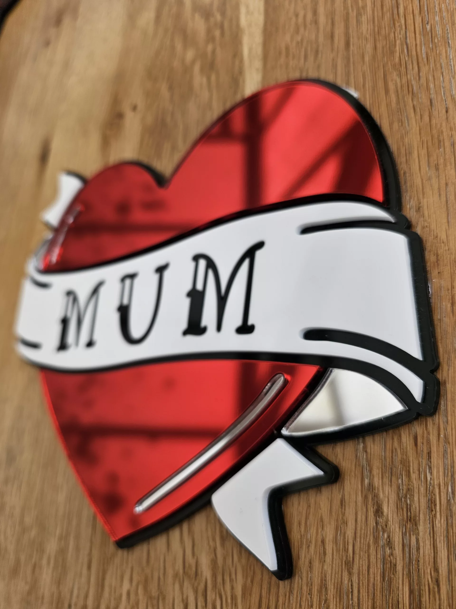 A handmade mirror in the shape of a heart with a banner running through the middle with the word mum. Made in an old school tattoo style.