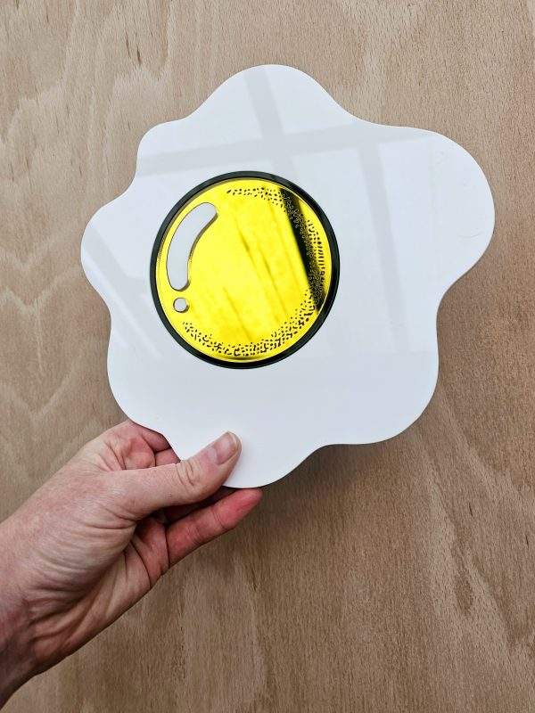 A piece of hand made wall art in the shape of an egg with a yellow mirrored yolk.