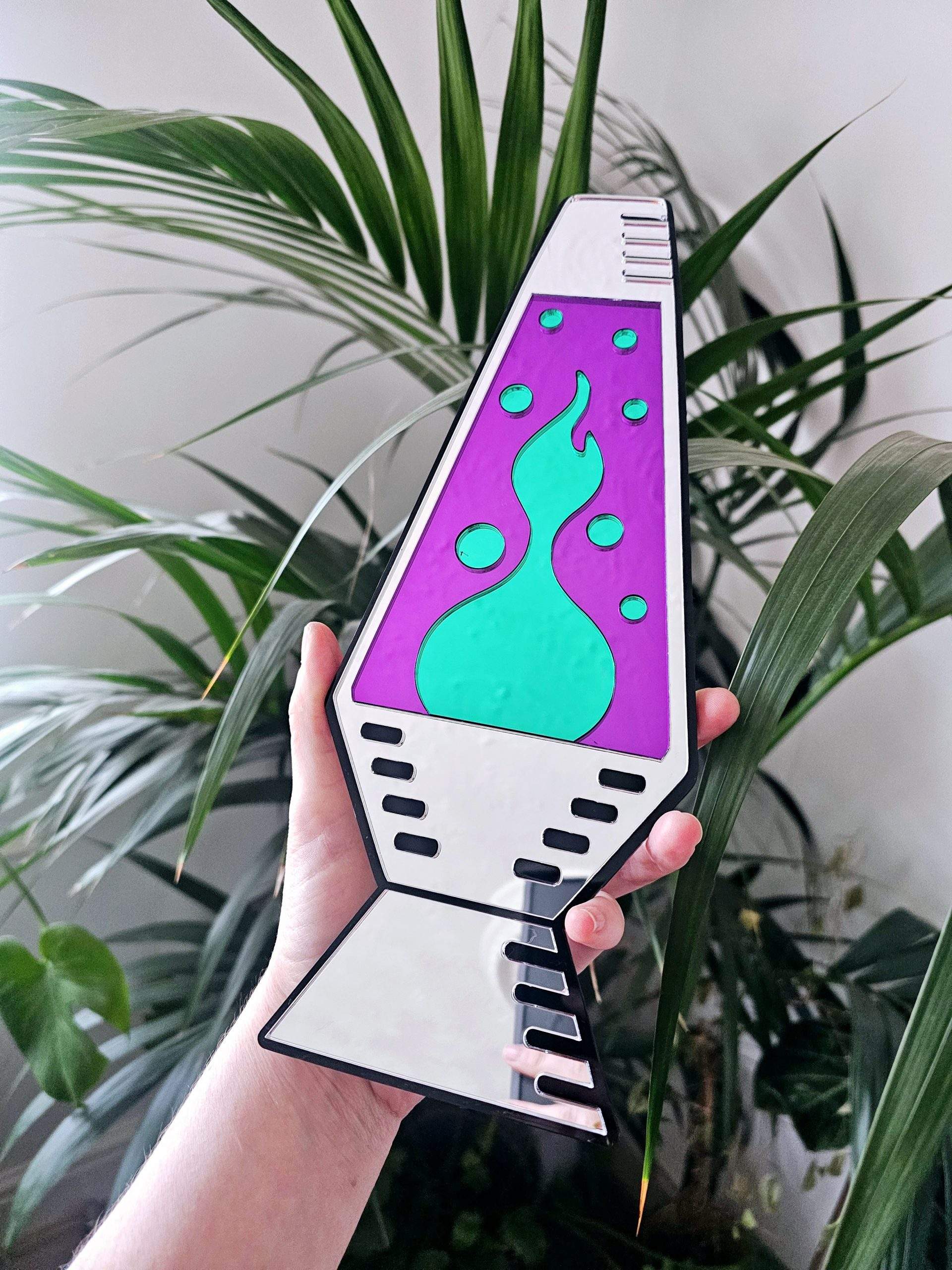 A mirror in the shape of a lava lamp. The lamp is silver, with purple and green 'liquid' pieces.