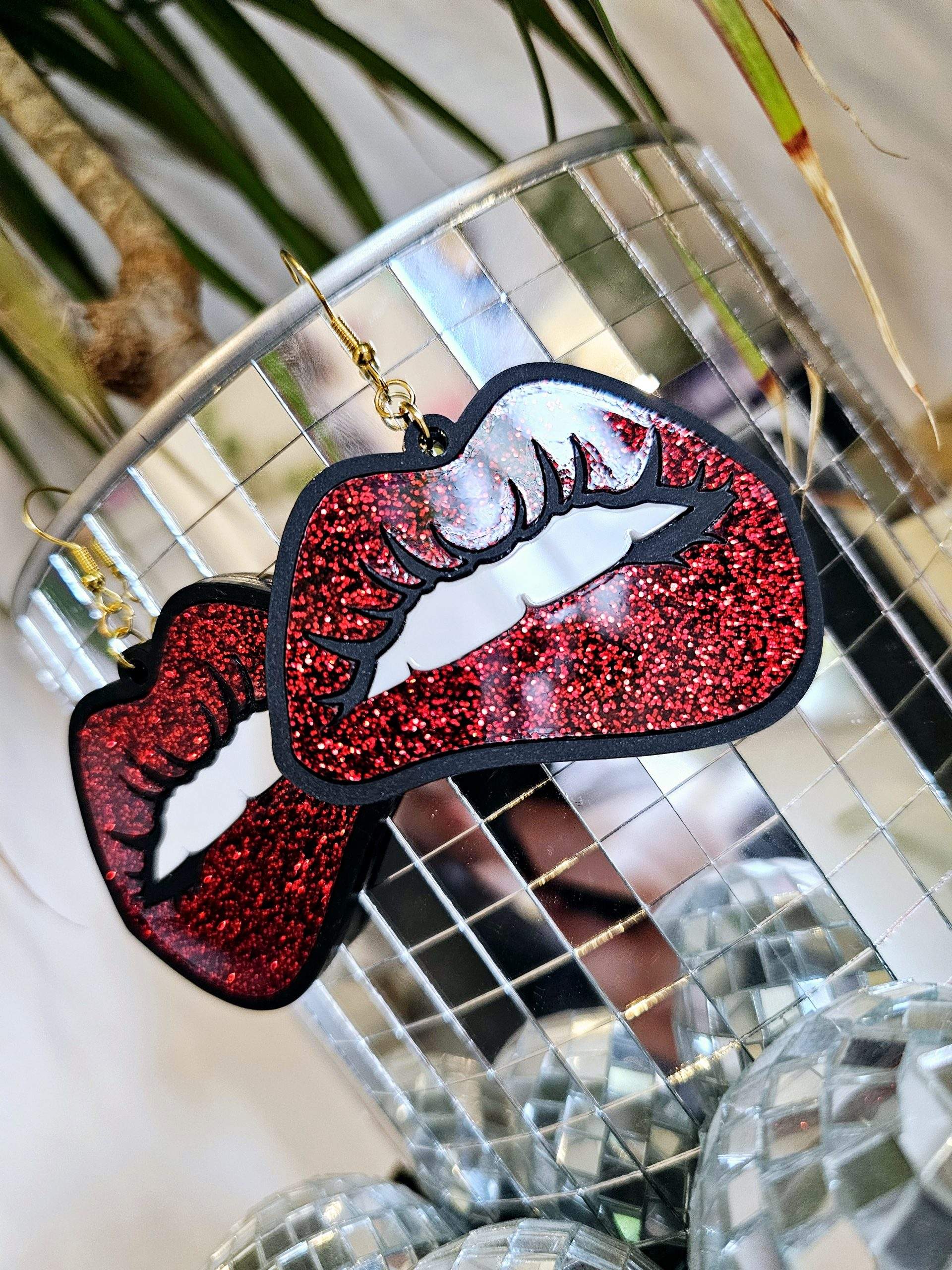 A pair of earrings in the shape of lips. They're in a pop art style with black outline and red glitter lips.