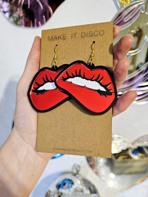 A pair of earrings in the shape of lips. They're in a pop art style with black outline and red mirror lips.