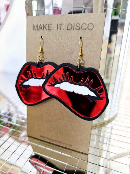 A pair of earrings in the shape of lips. They're in a pop art style with black outline and red mirror lips.