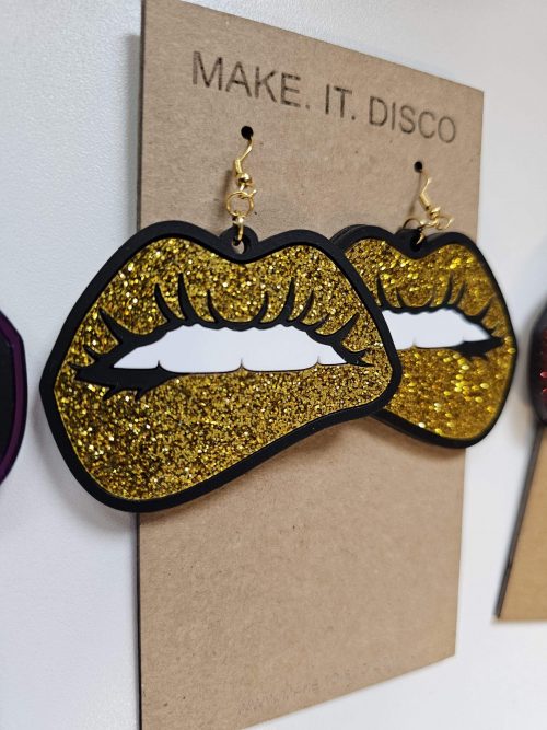 A pair of earrings in the shape of lips. They're in a pop art style with black outline and gold glitter lips.