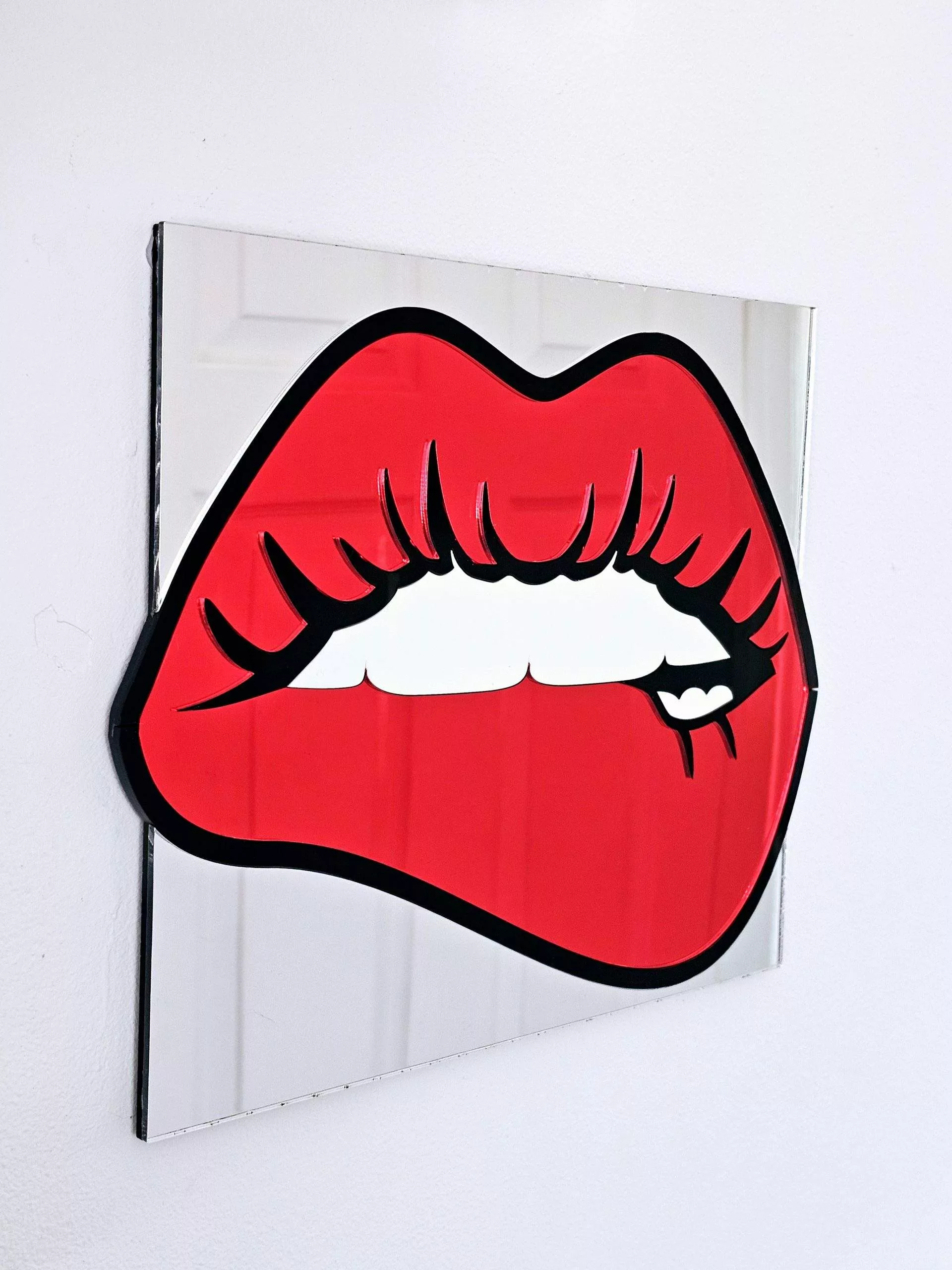 A handmade mirrorin the shape of lips. The lips are made in a pop art style with a black outline and red mirror lips.