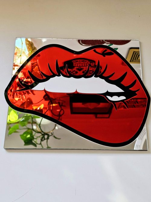A handmade mirrorin the shape of lips. The lips are made in a pop art style with a black outline and red mirror lips.