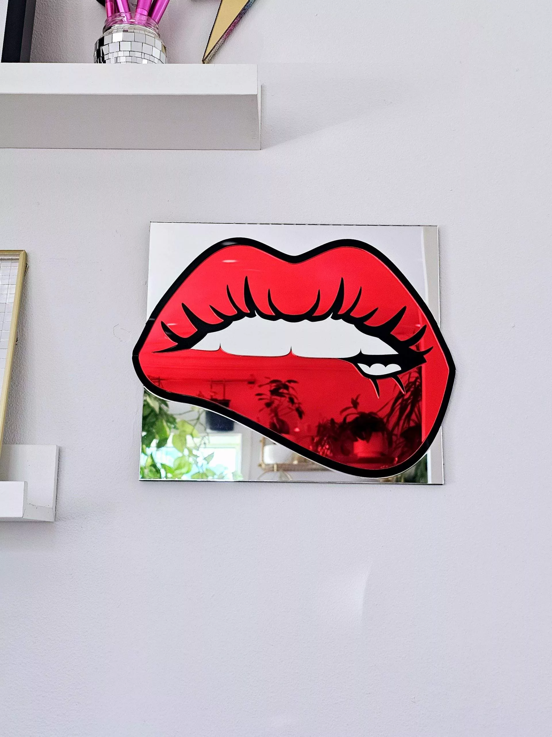 A handmade mirrorin the shape of lips. The lips are made in a pop art style with a black outline and red mirror lips.