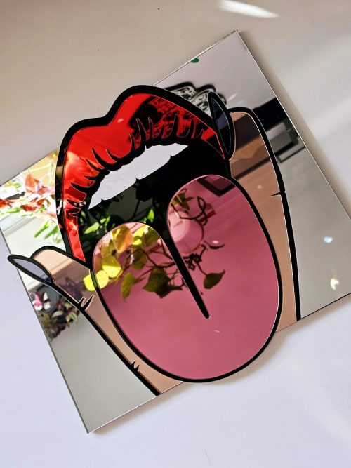 A handmade mirror in the shape of a mouth making a rude gesture, with tongue out and fingers either side.