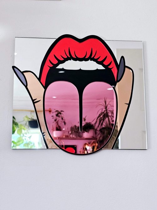 A handmade mirror in the shape of a mouth making a rude gesture, with tongue out and fingers either side.