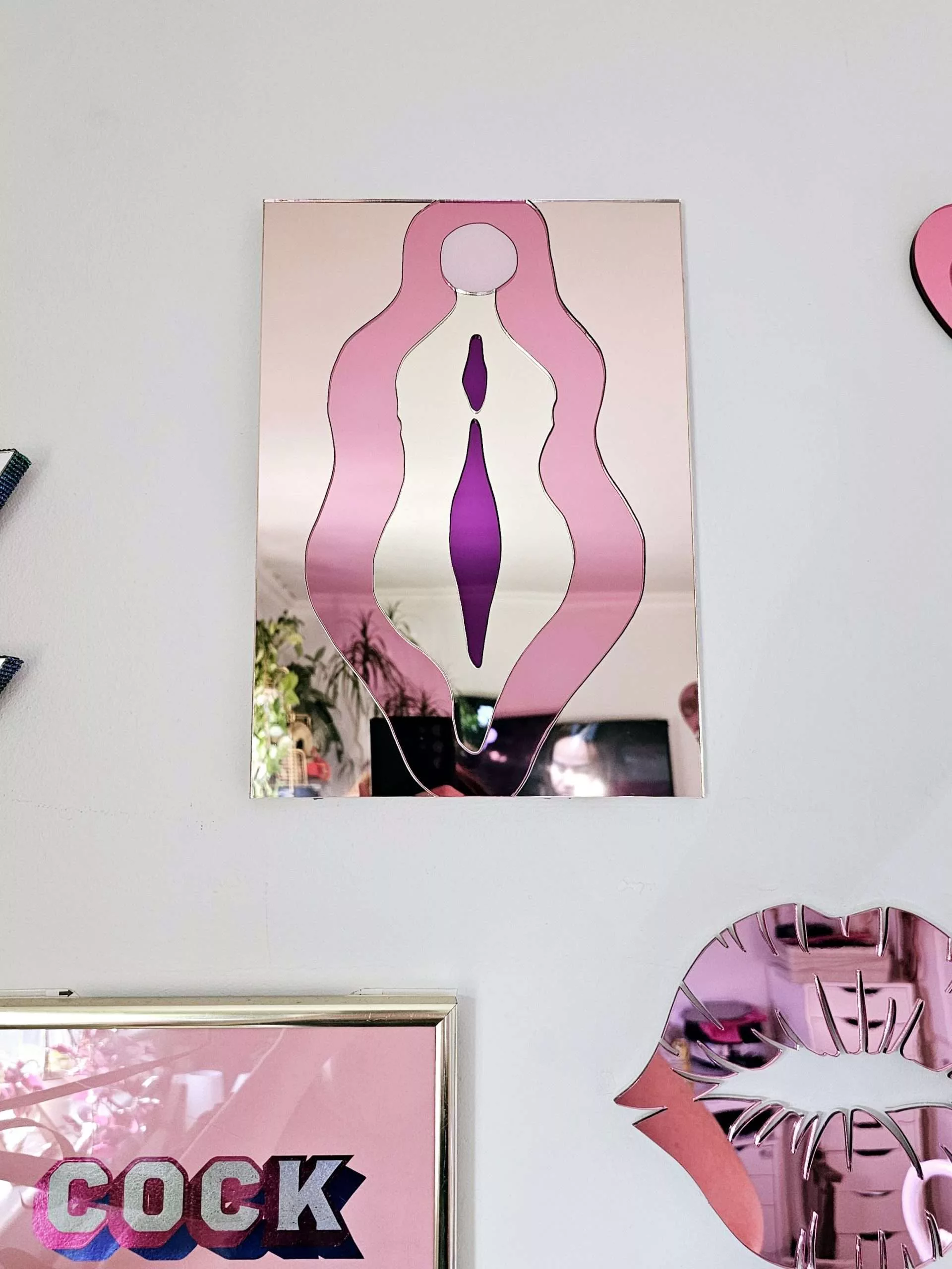 A mirror in the design of a vulva. The mirror is made from pieces of rose gold, pink, gold and purple mirror.