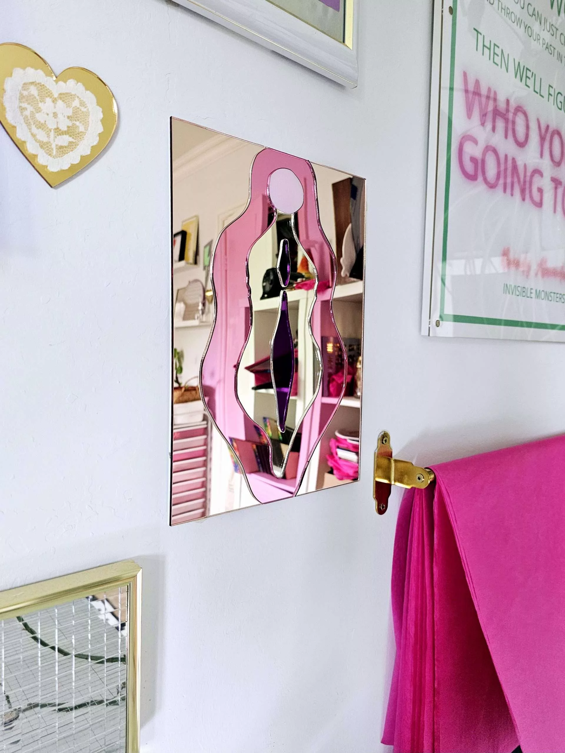 A mirror in the design of a vulva. The mirror is made from pieces of rose gold, pink, gold and purple mirror.
