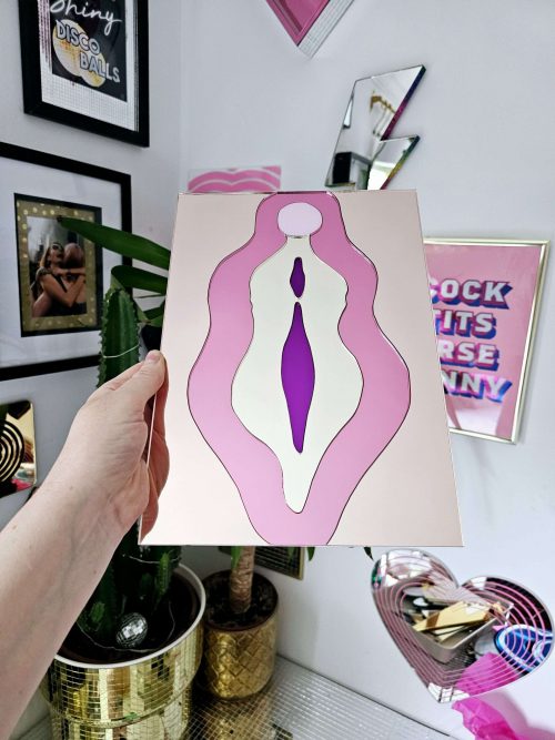 A mirror in the design of a vulva. The mirror is made from pieces of rose gold, pink, gold and purple mirror.