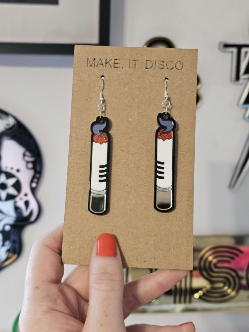 A pair of handmade earrings in the shape of a cigarette. Made from gloss and mirror acrylic, with black outline details.