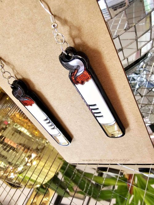 A pair of handmade earrings in the shape of a cigarette. Made from gloss and mirror acrylic, with black outline details.