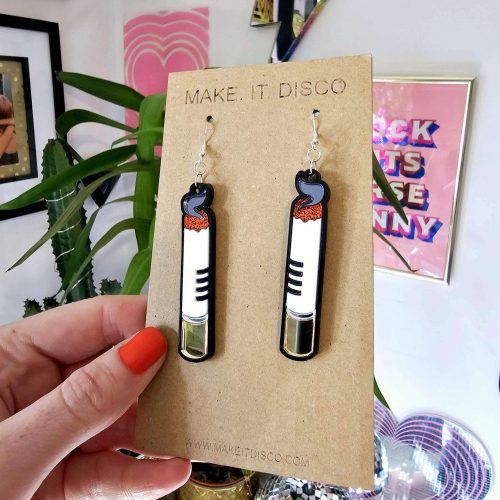 A pair of handmade earrings in the shape of a cigarette. Made from gloss and mirror acrylic, with black outline details.