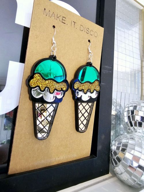 Handmade earrings in the shape of an ice cream. The earrings have a black outline, filled with mirror and gltter acrylic pieces.
