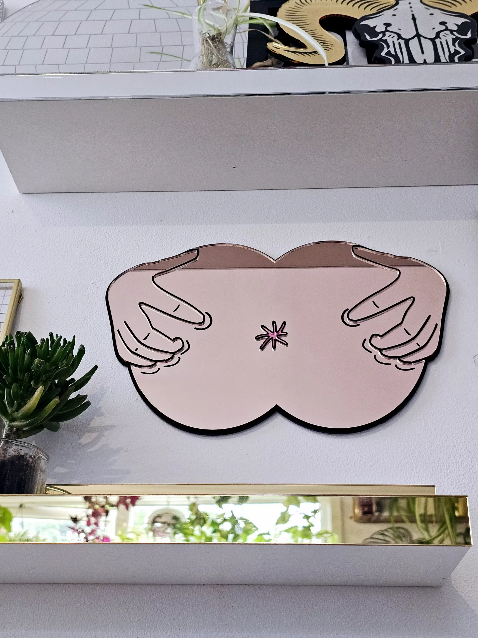 A handmade mirror in the shape of a butthole. The mirror hands pulling the butthole open.