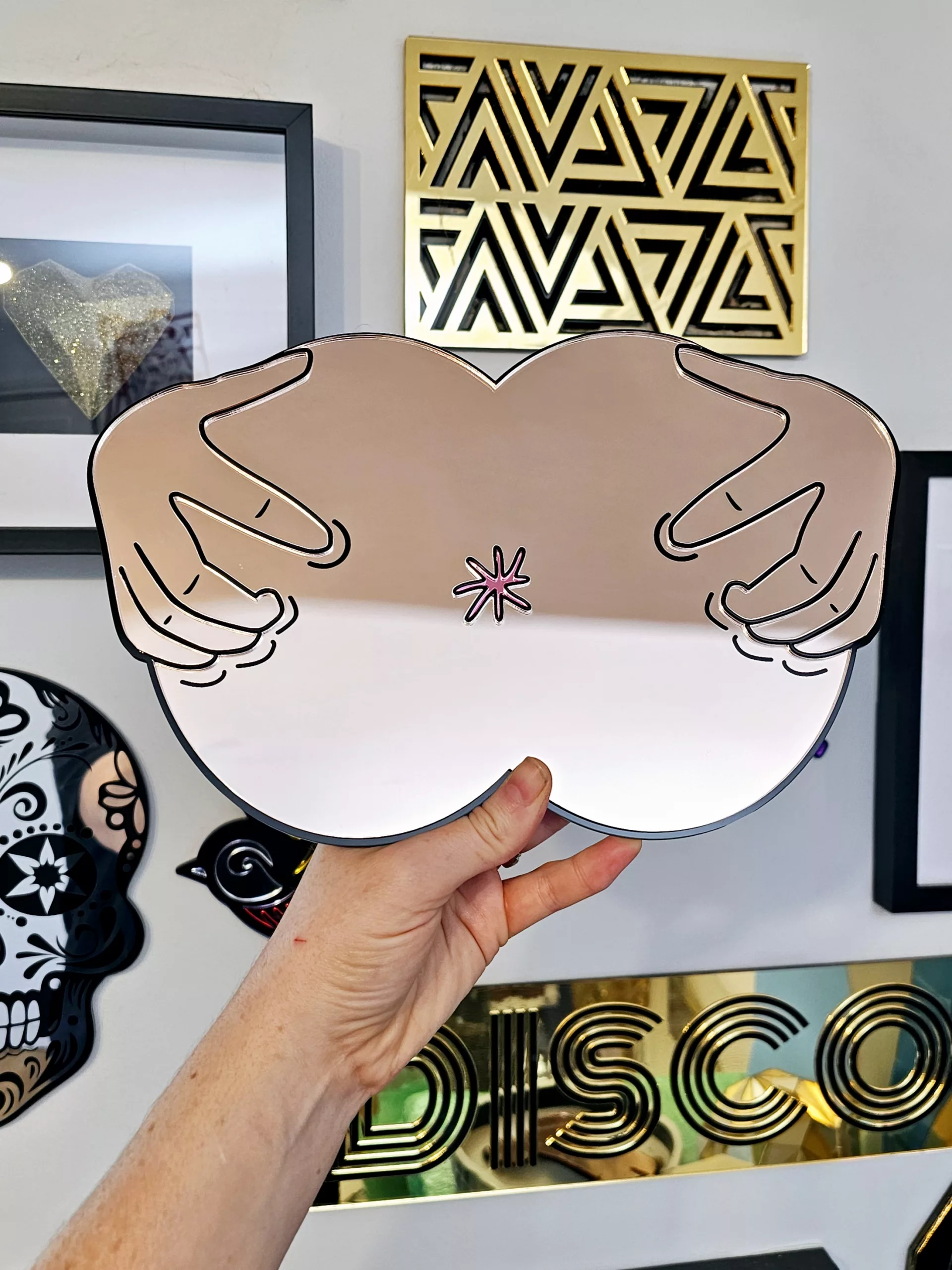 A handmade mirror in the shape of a butthole. The mirror hands pulling the butthole open.