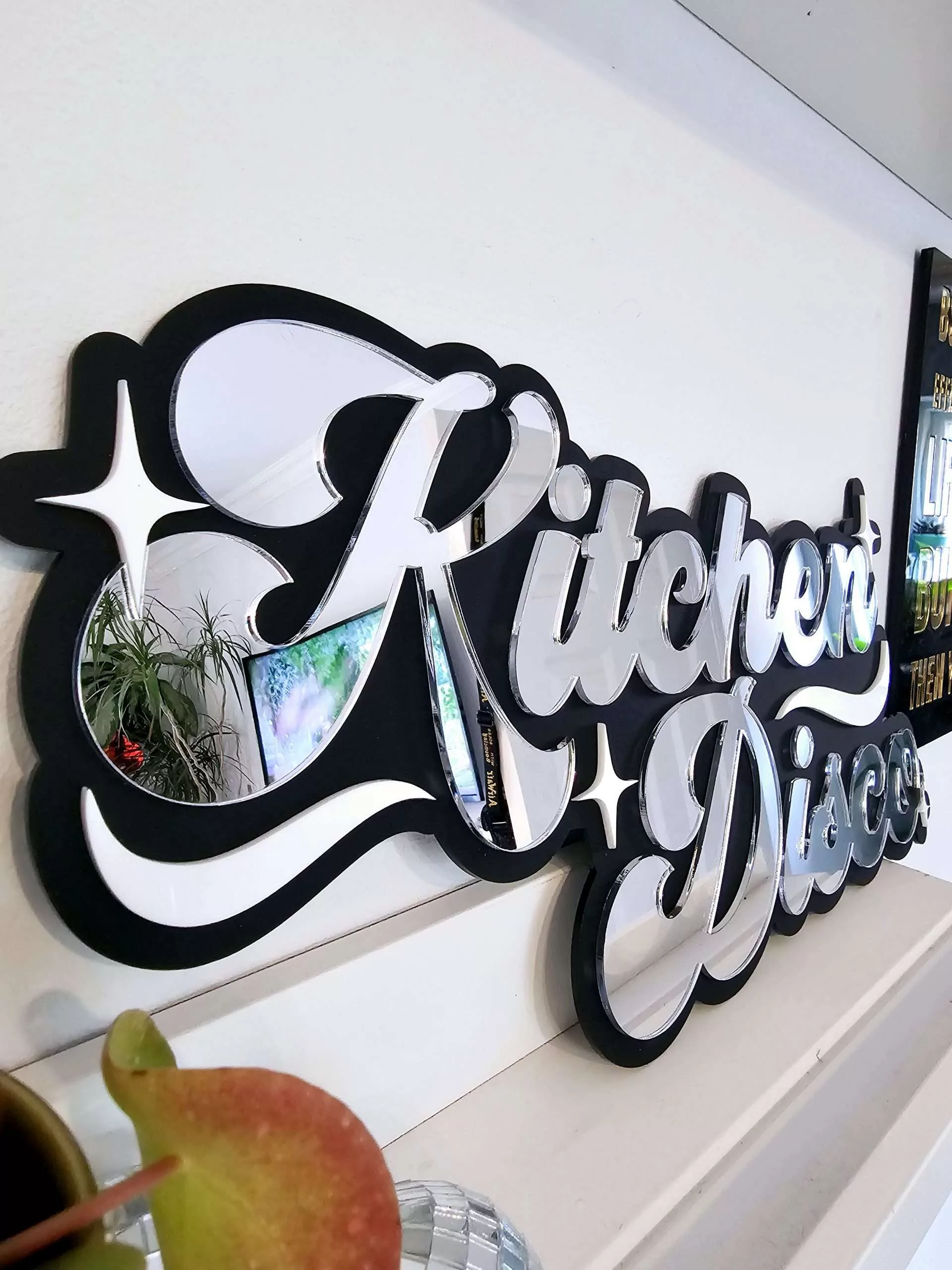 A sign that says Kitchen Disco. Made with a black backing and silver lettering.