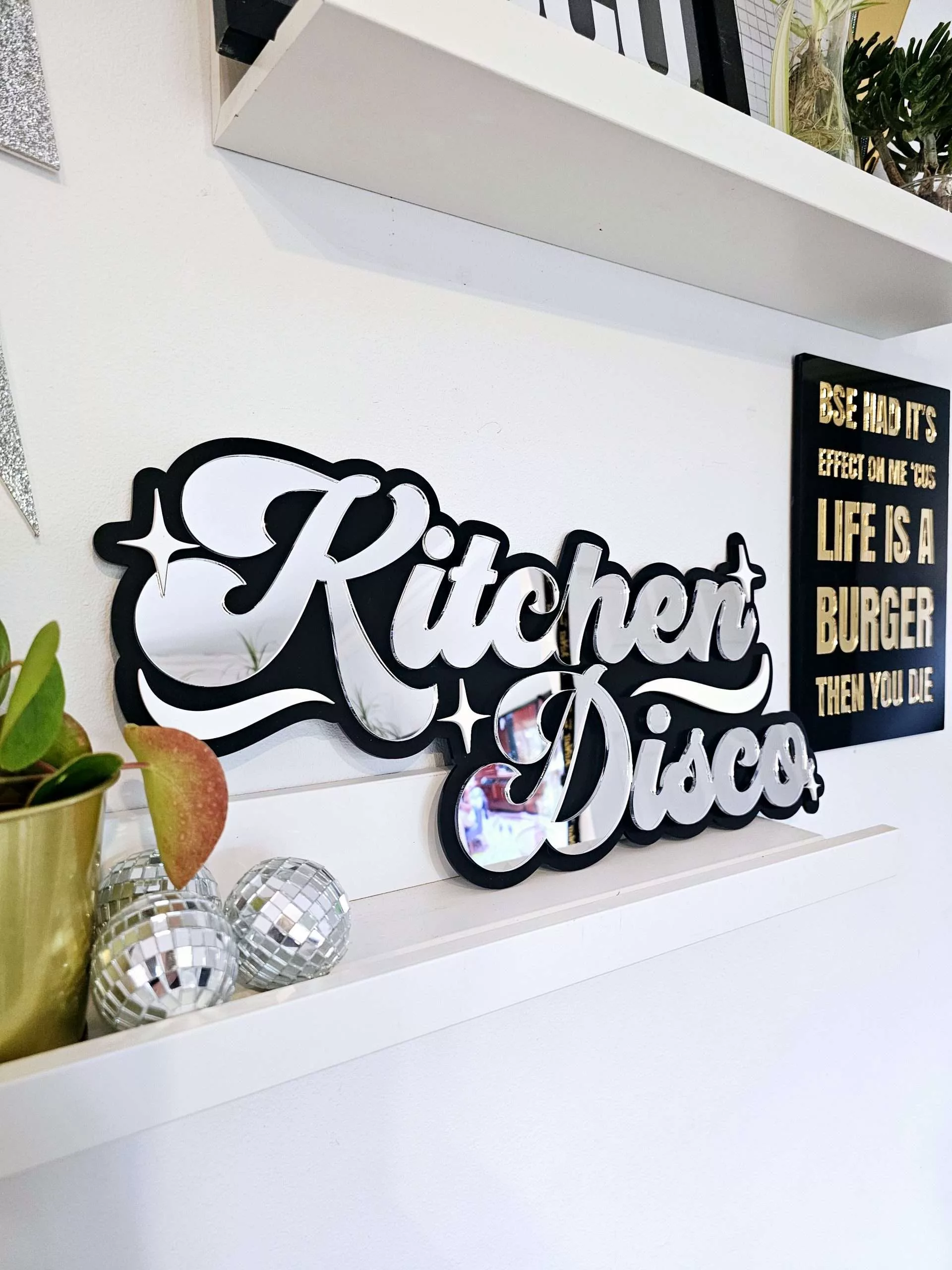 A sign that says Kitchen Disco. Made with a black backing and silver lettering.