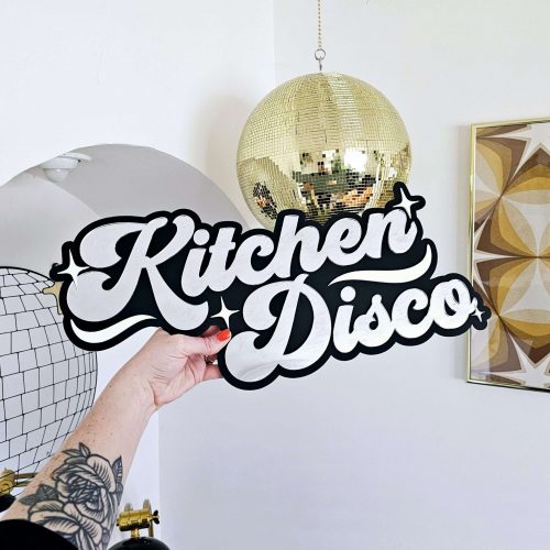 A sign that says Kitchen Disco. Made with a black backing and silver lettering.