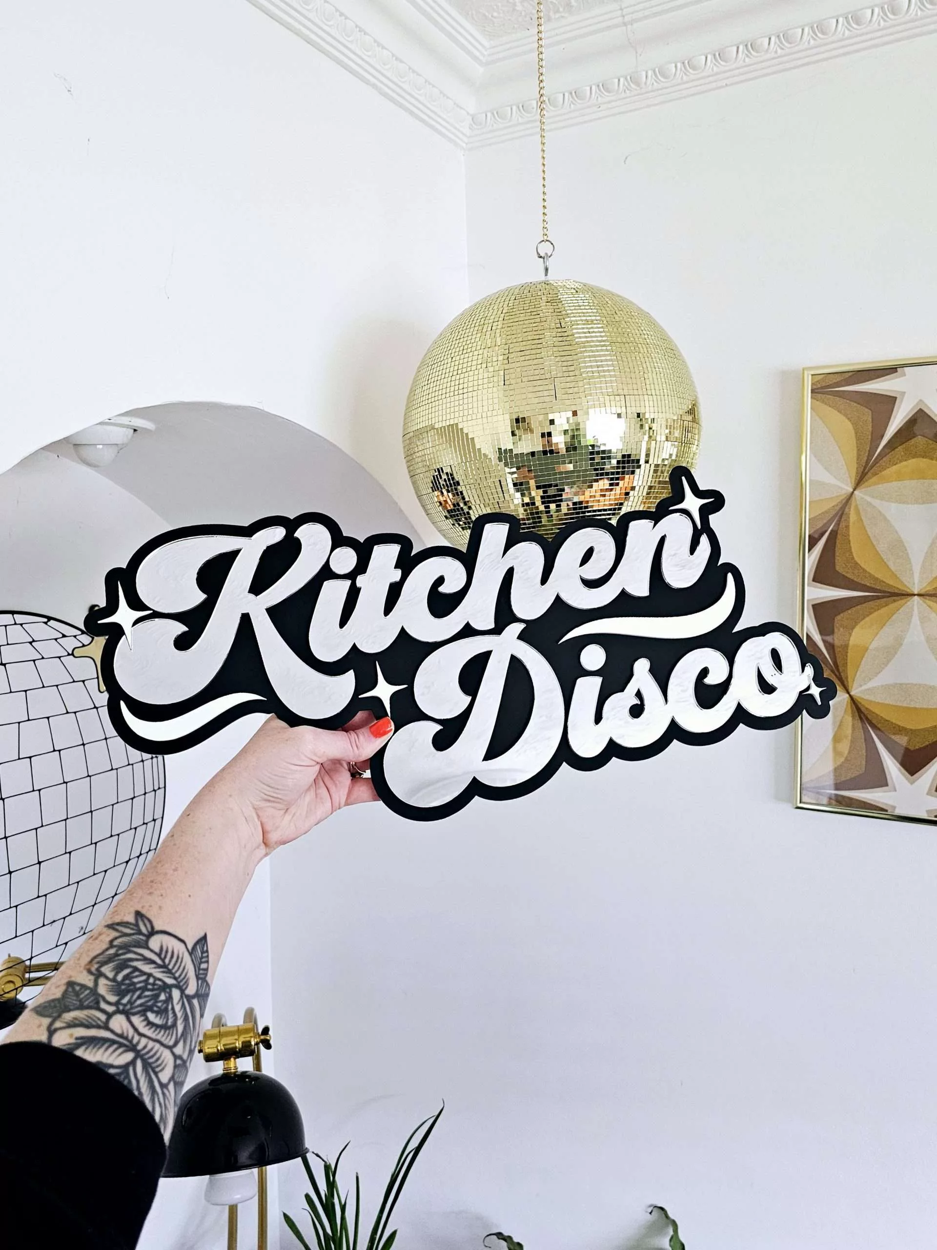 A sign that says Kitchen Disco. Made with a black backing and silver lettering.