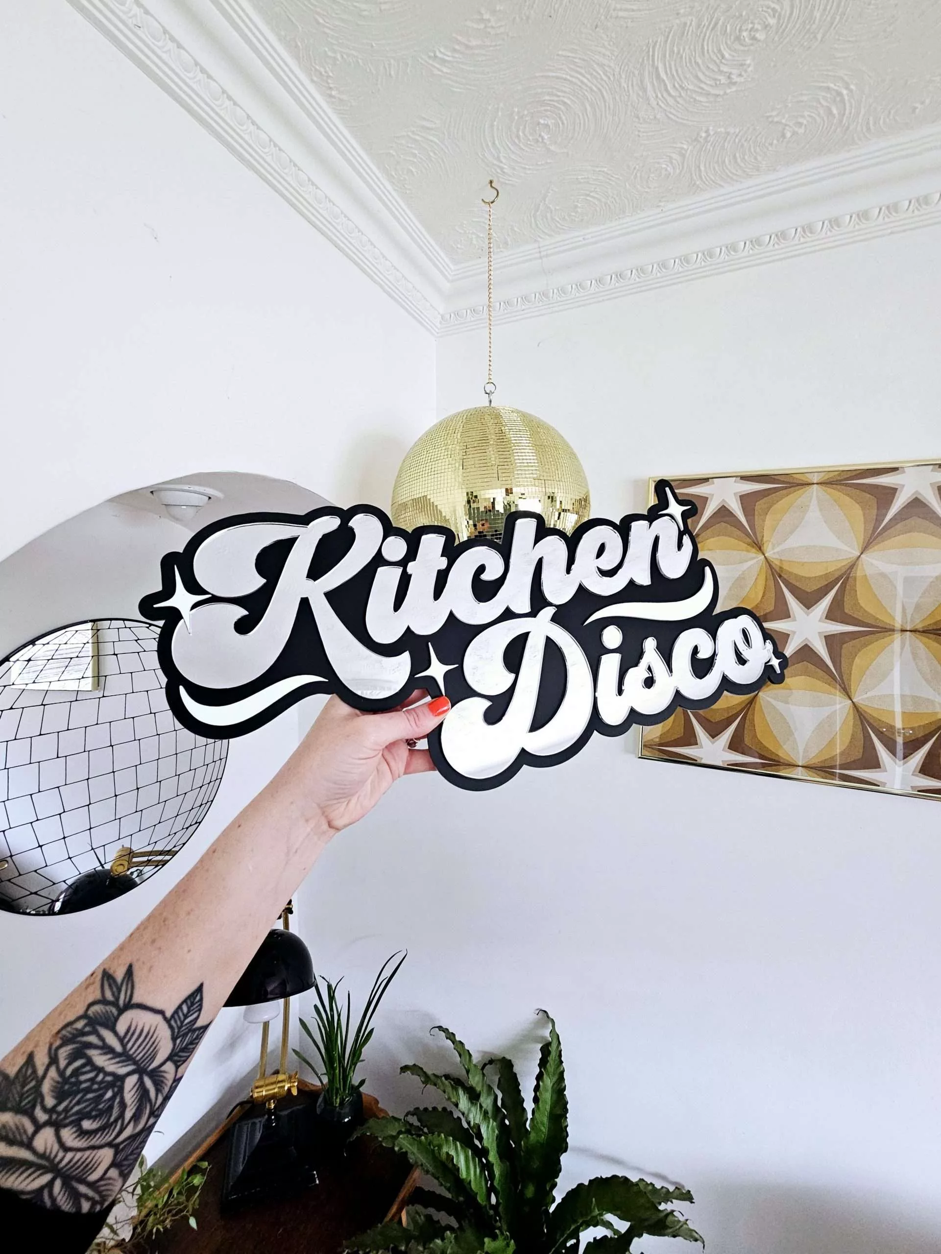 A sign that says Kitchen Disco. Made with a black backing and silver lettering.