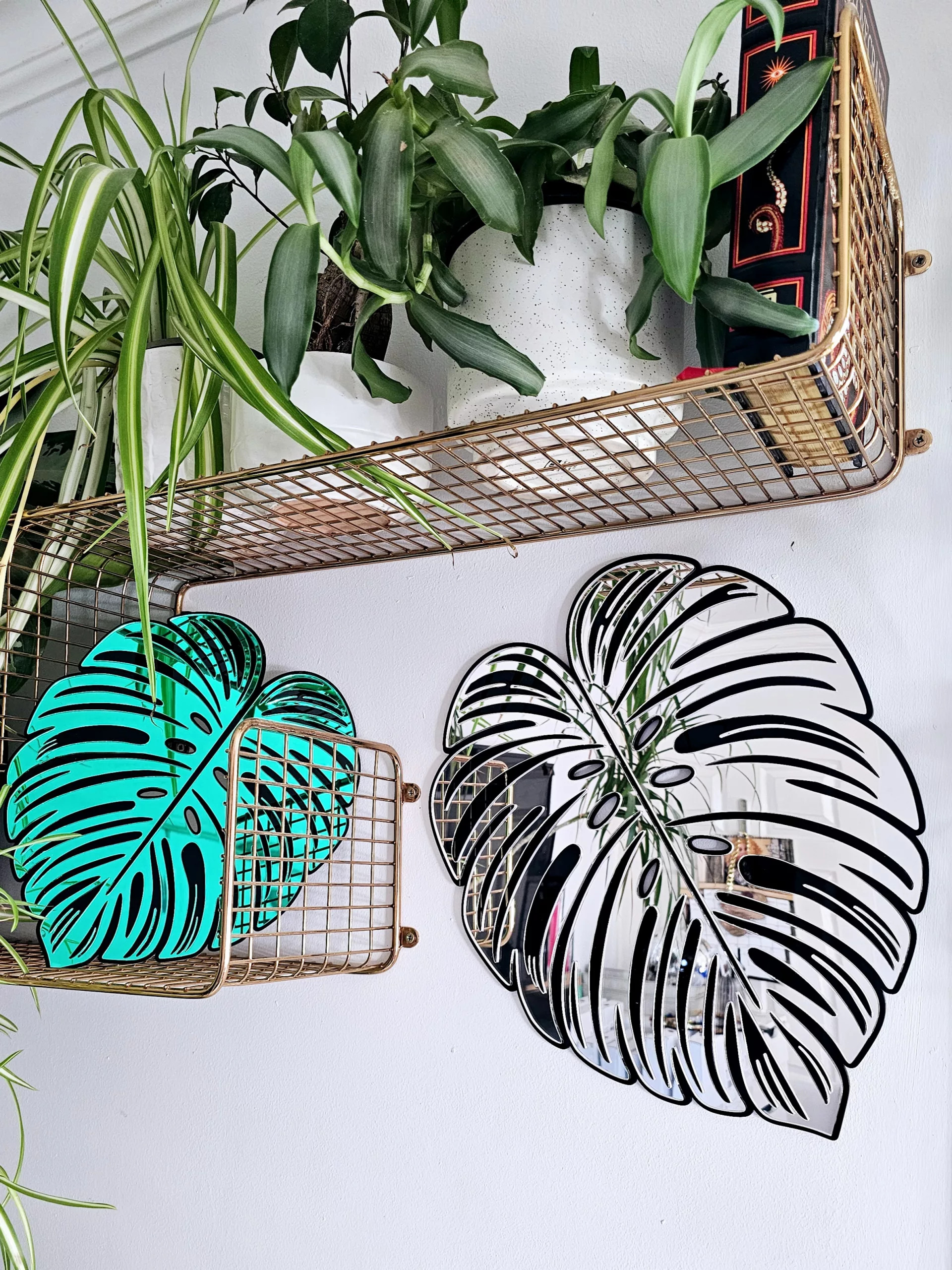 A handmade mirror in the shape of a monstera leaf. The mirror has a black outline, with green and silver mirror leaves.