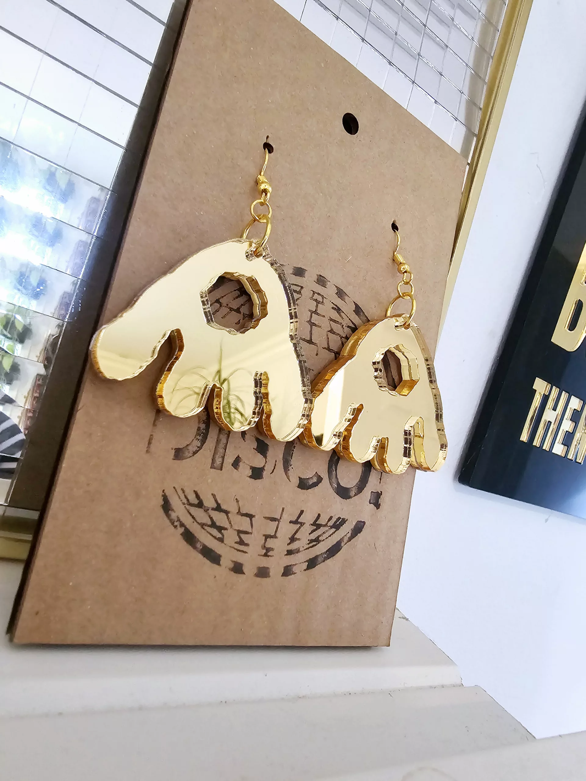 A pair of handmade earrings in the shape of the monster munch snack, made from gold mirrored acrylic.
