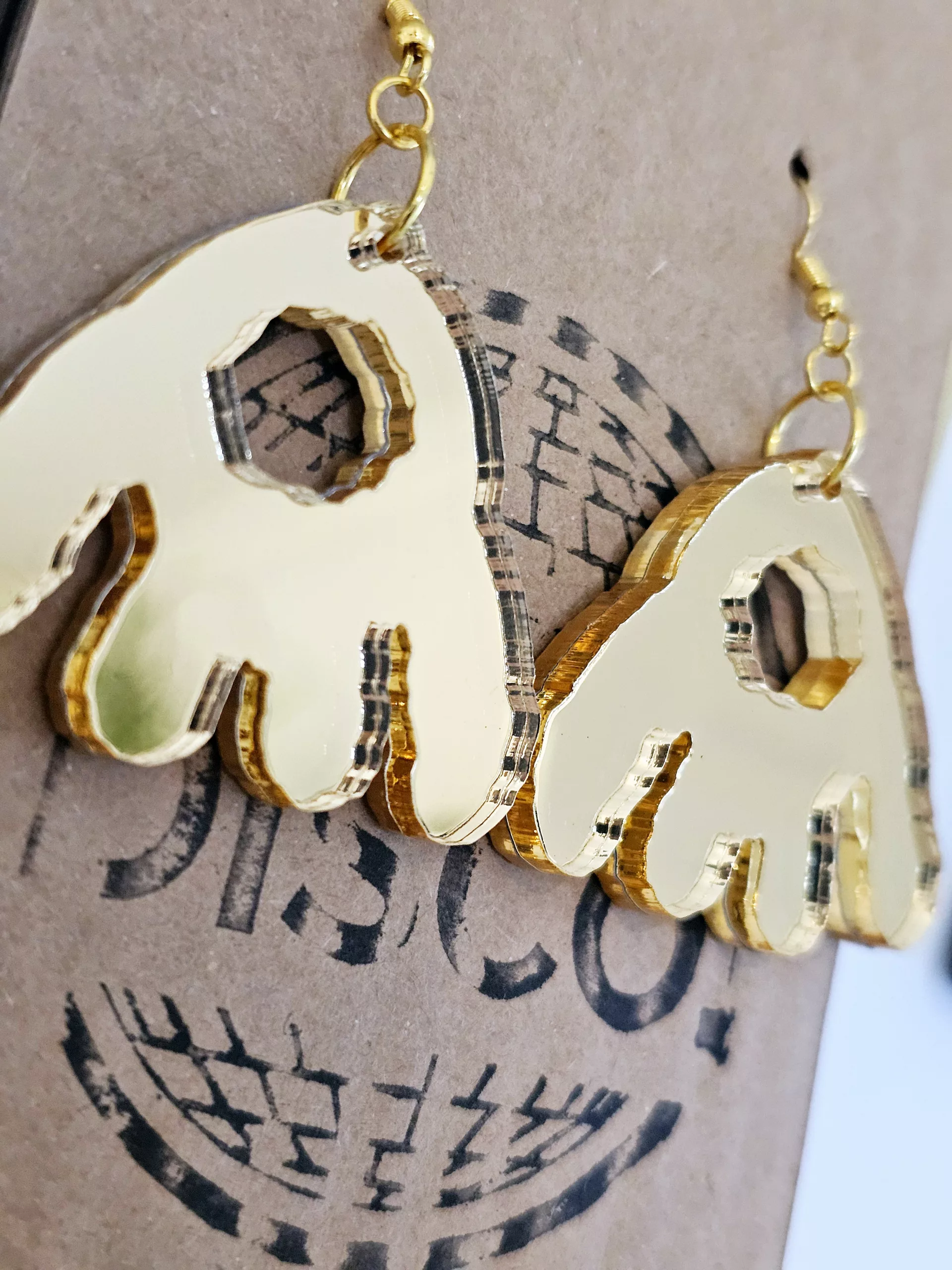 A pair of handmade earrings in the shape of the monster munch snack, made from gold mirrored acrylic.