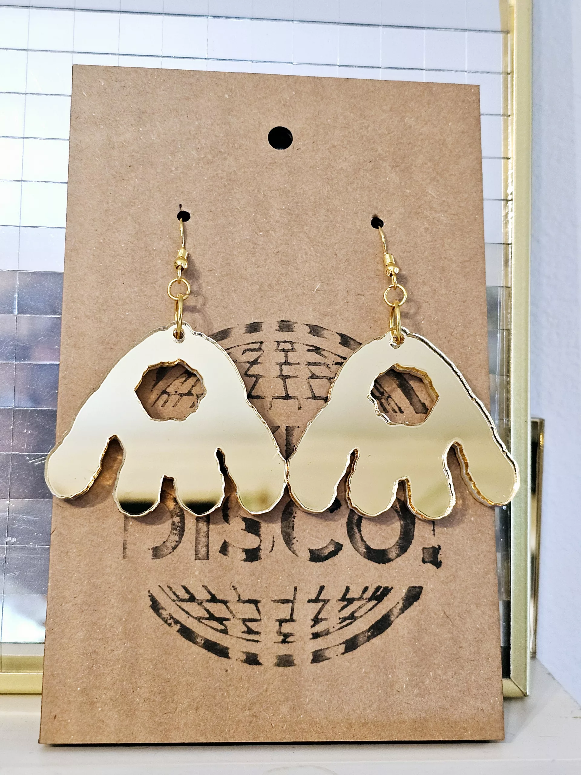A pair of handmade earrings in the shape of the monster munch snack, made from gold mirrored acrylic.