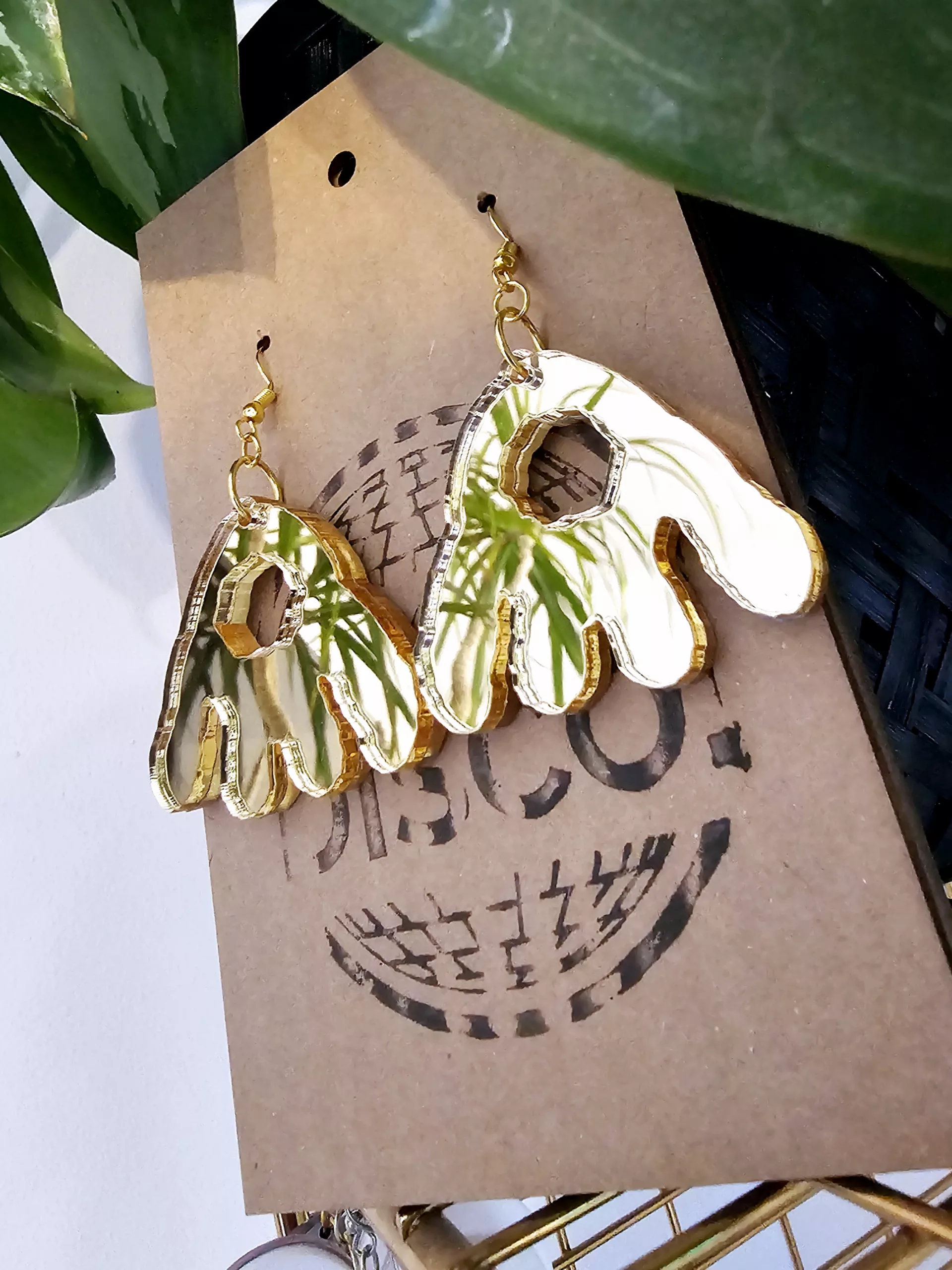 A pair of handmade earrings in the shape of the monster munch snack, made from gold mirrored acrylic.