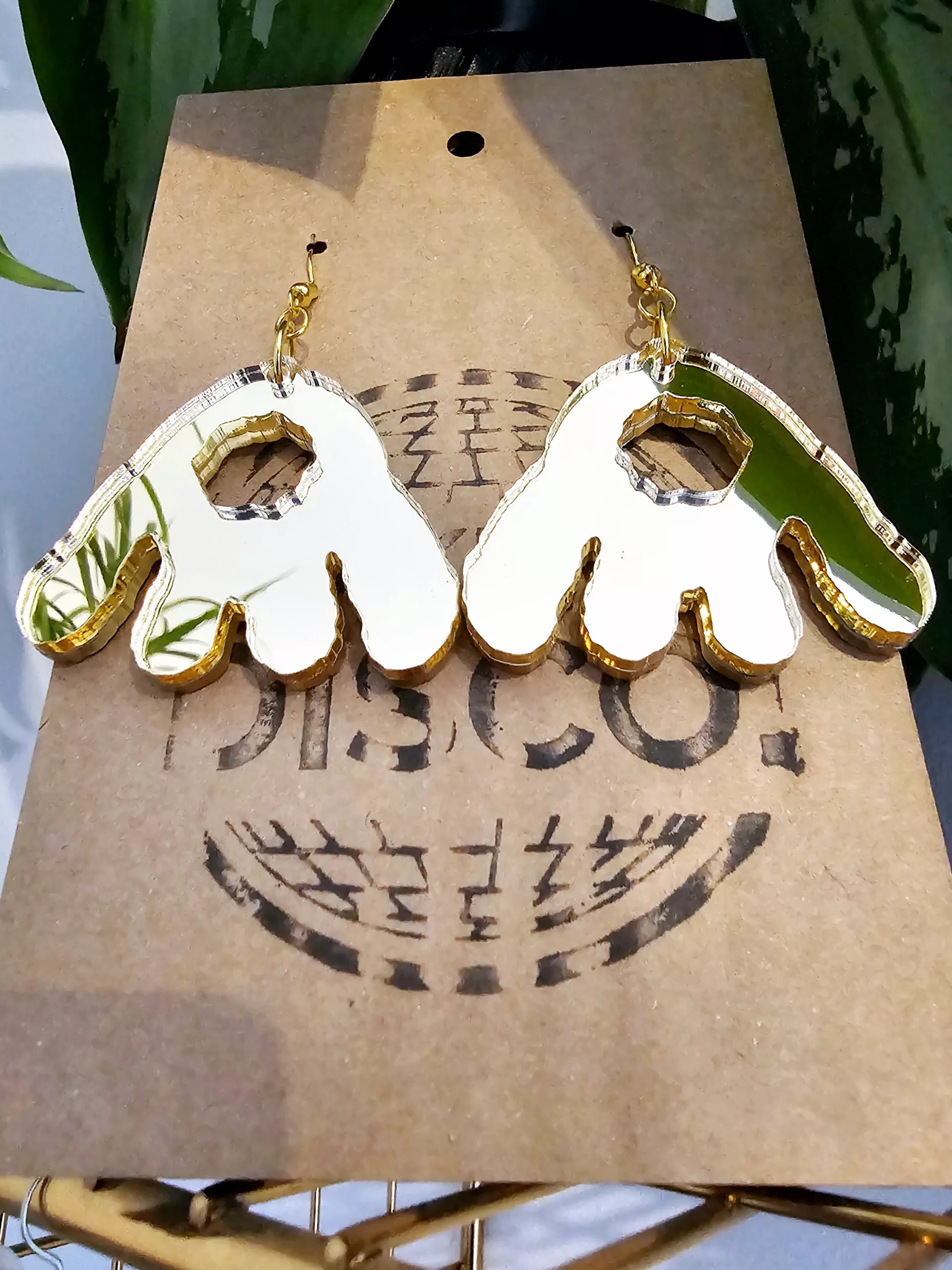 A pair of handmade earrings in the shape of the monster munch snack, made from gold mirrored acrylic.