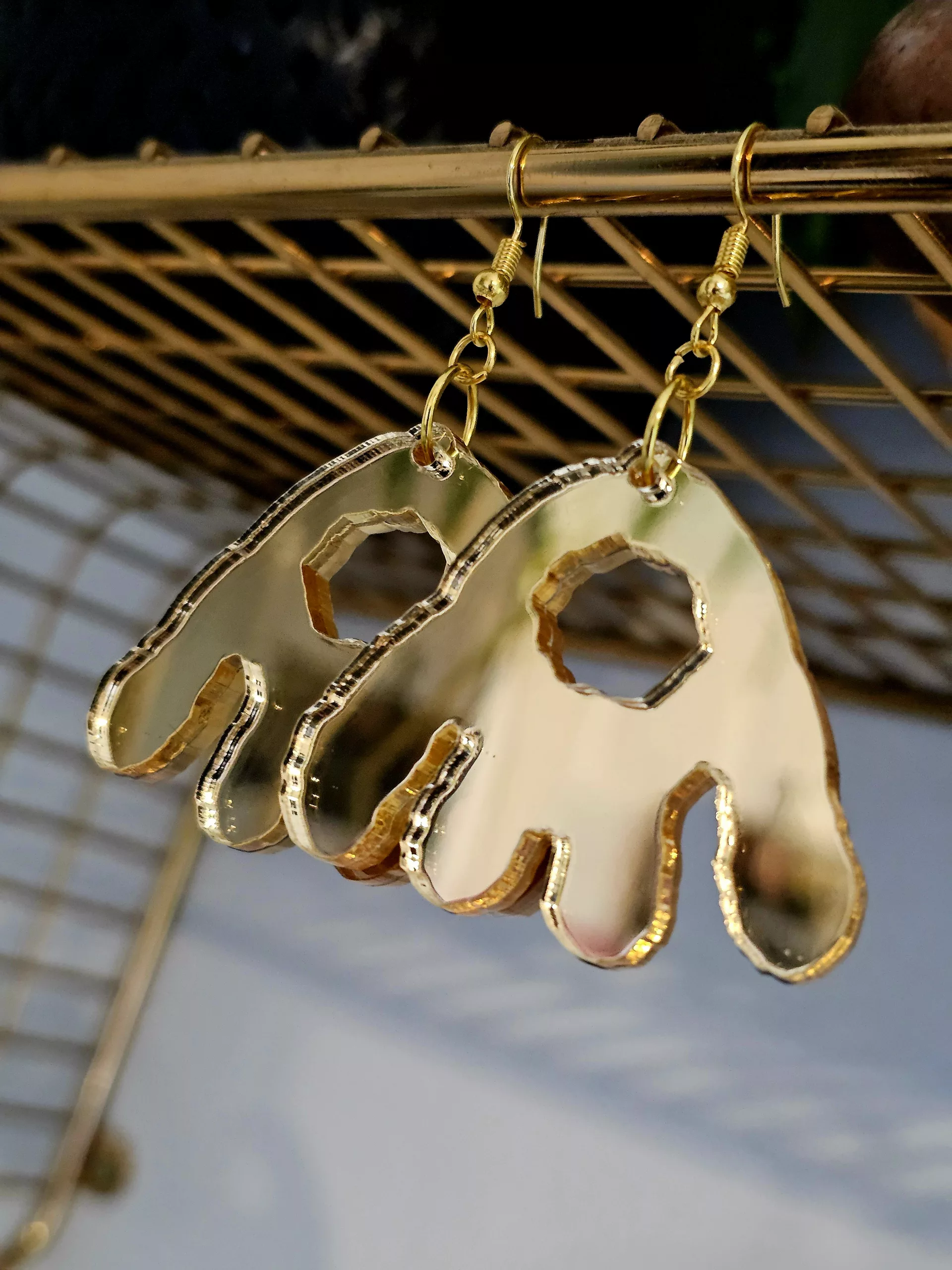 A pair of handmade earrings in the shape of the monster munch snack, made from gold mirrored acrylic.