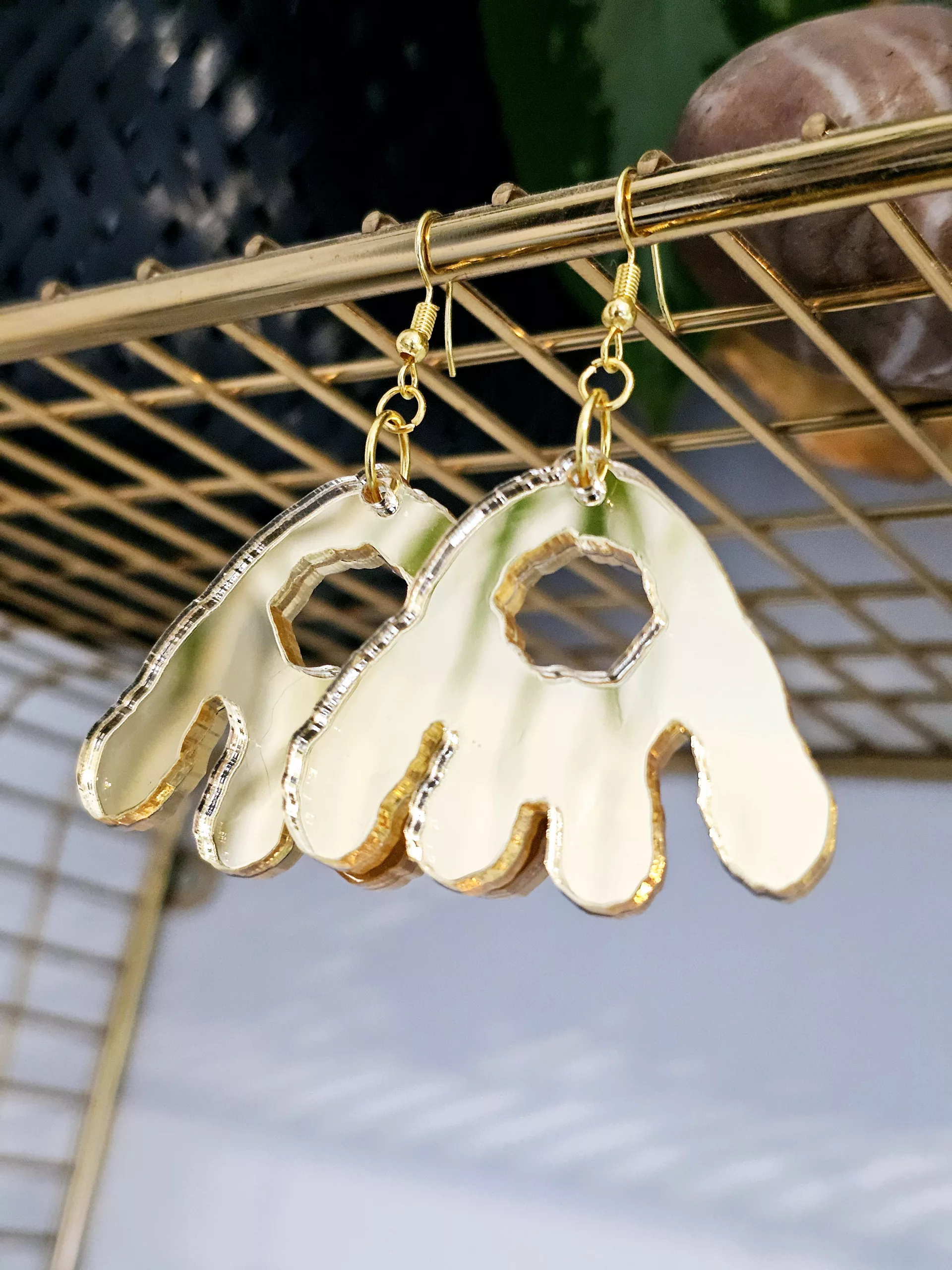 A pair of handmade earrings in the shape of the monster munch snack, made from gold mirrored acrylic.