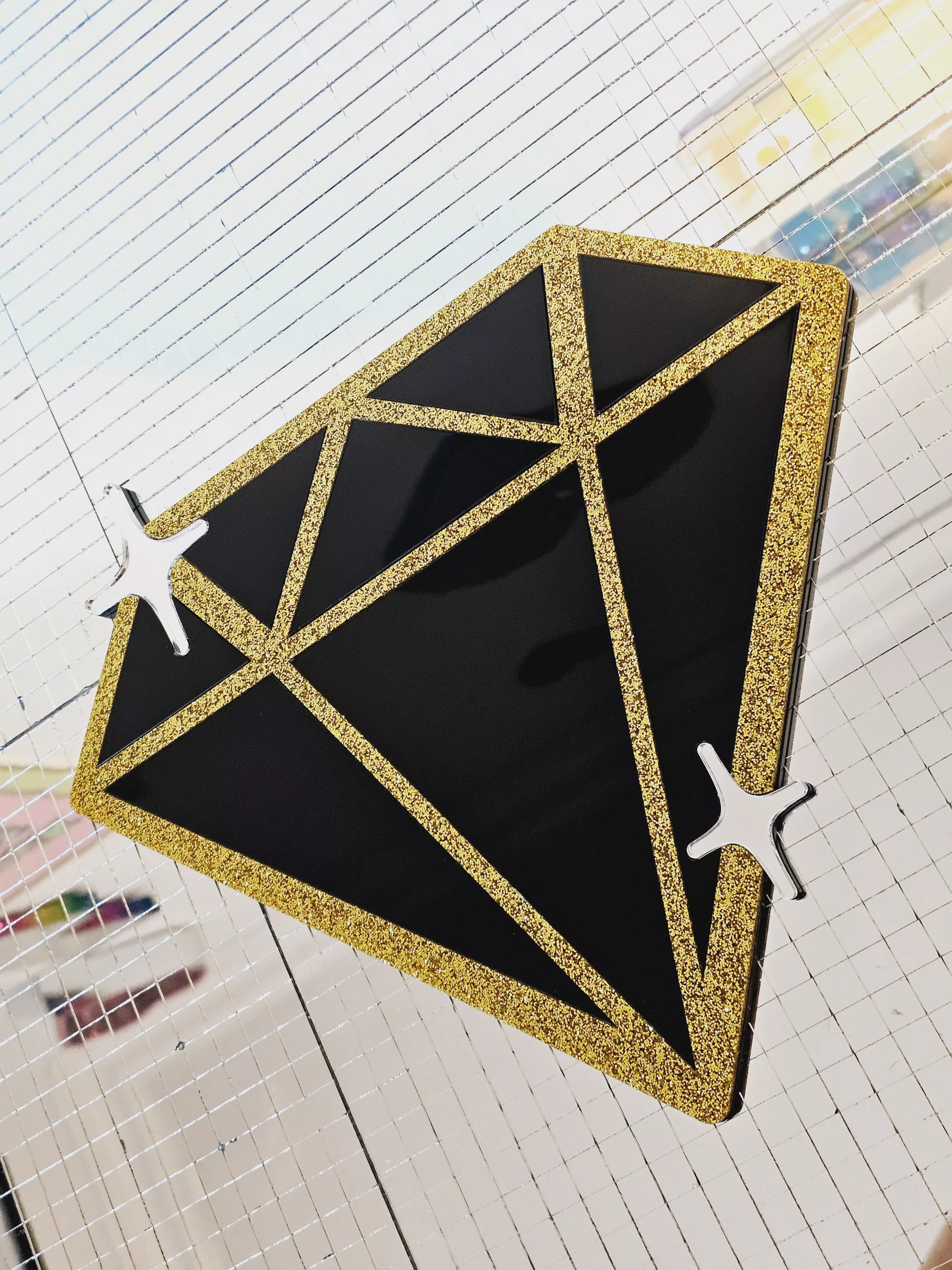 A piece of handmade wall afrt in the shape of a diamond with black gloss pieces and gold glitter outline,