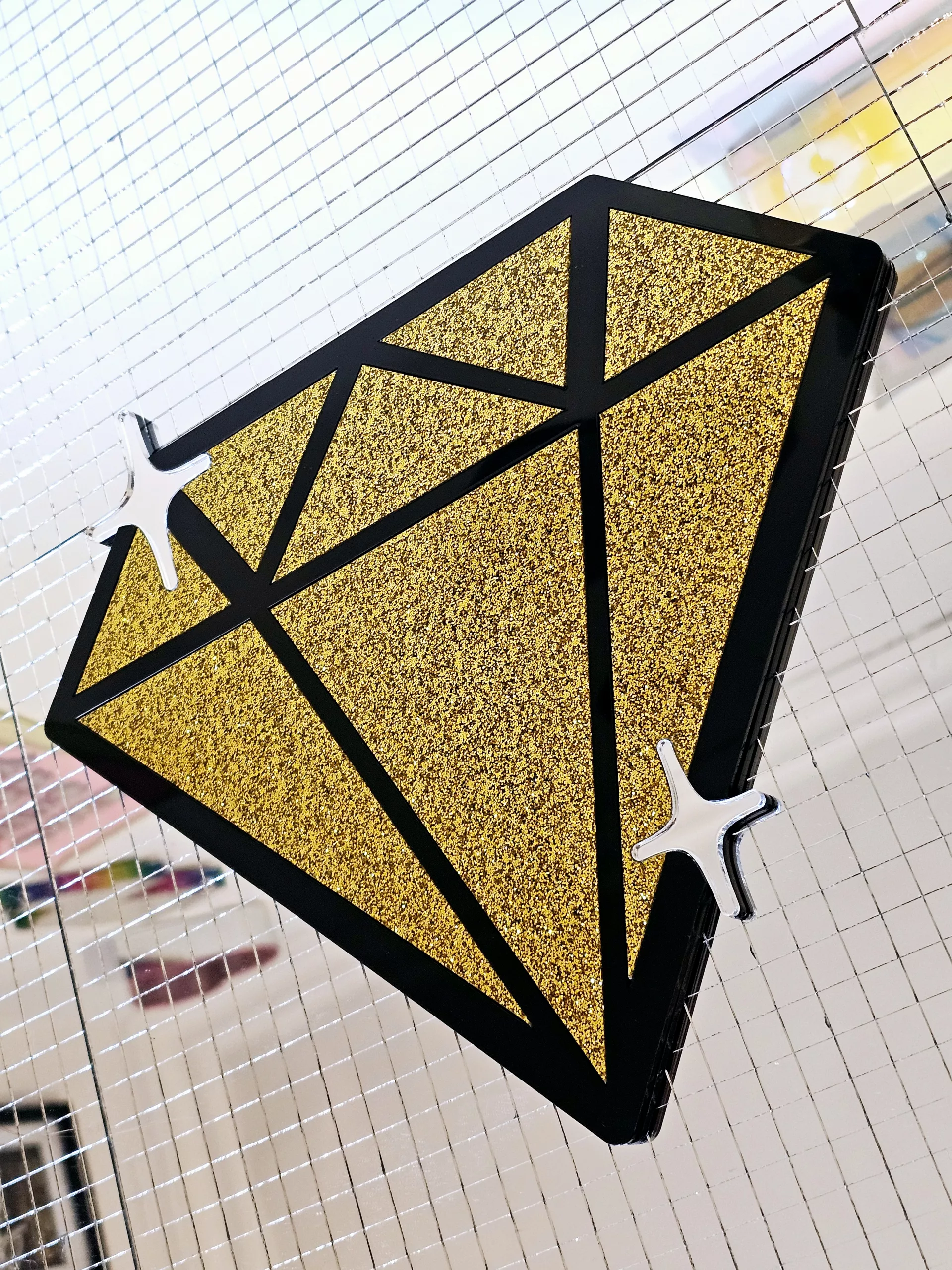 A piece of handmade wall afrt in the shape of a diamond with gold glitter pieces and a black gloss outline,