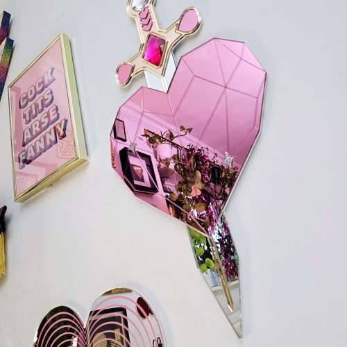 A handmade mirror on the shape of a sword piercing a heart. Made with gold, rose gold, pink and silver mirror with gem accents.