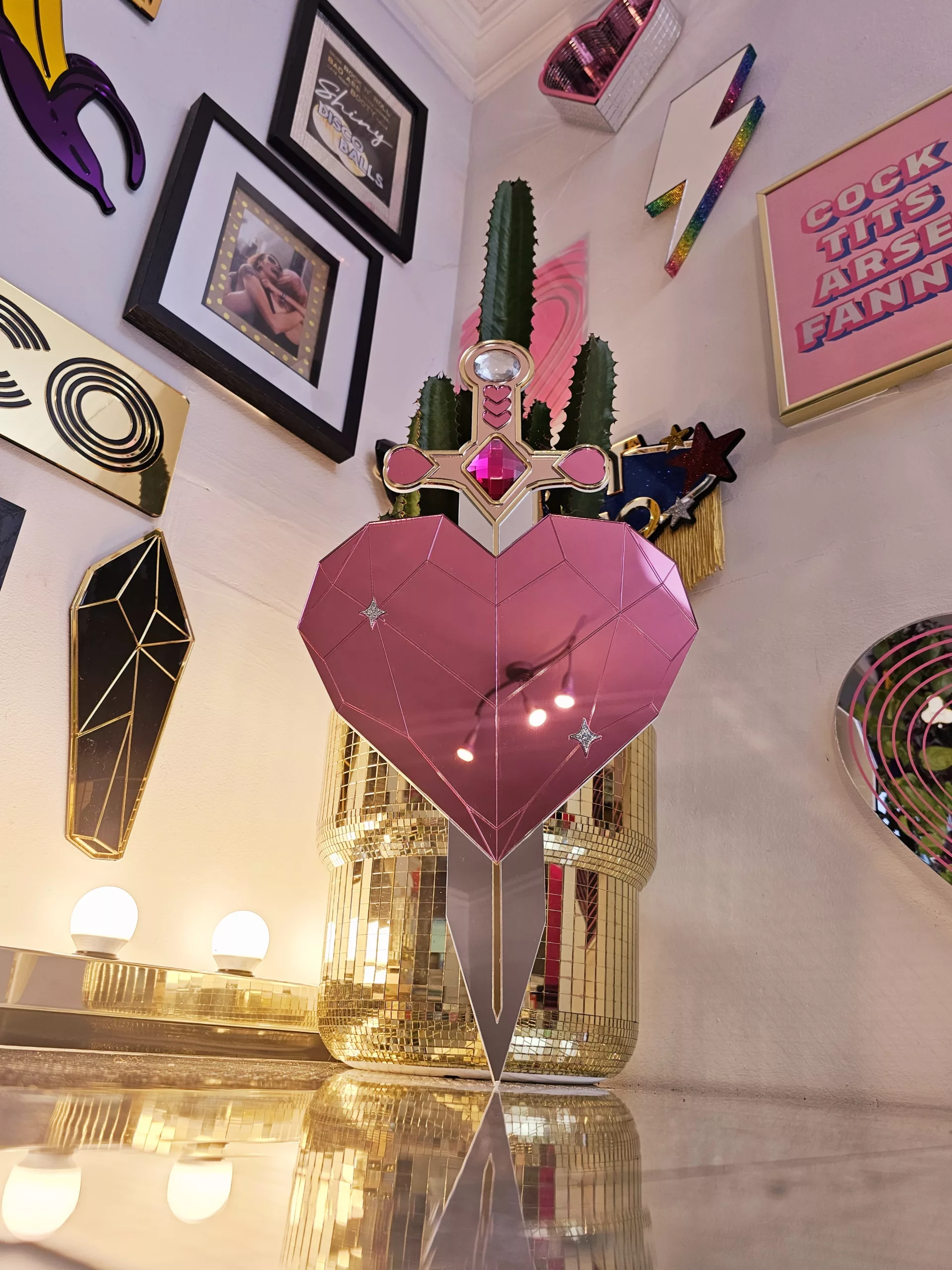 A handmade mirror on the shape of a sword piercing a heart. Made with gold, rose gold, pink and silver mirror with gem accents.
