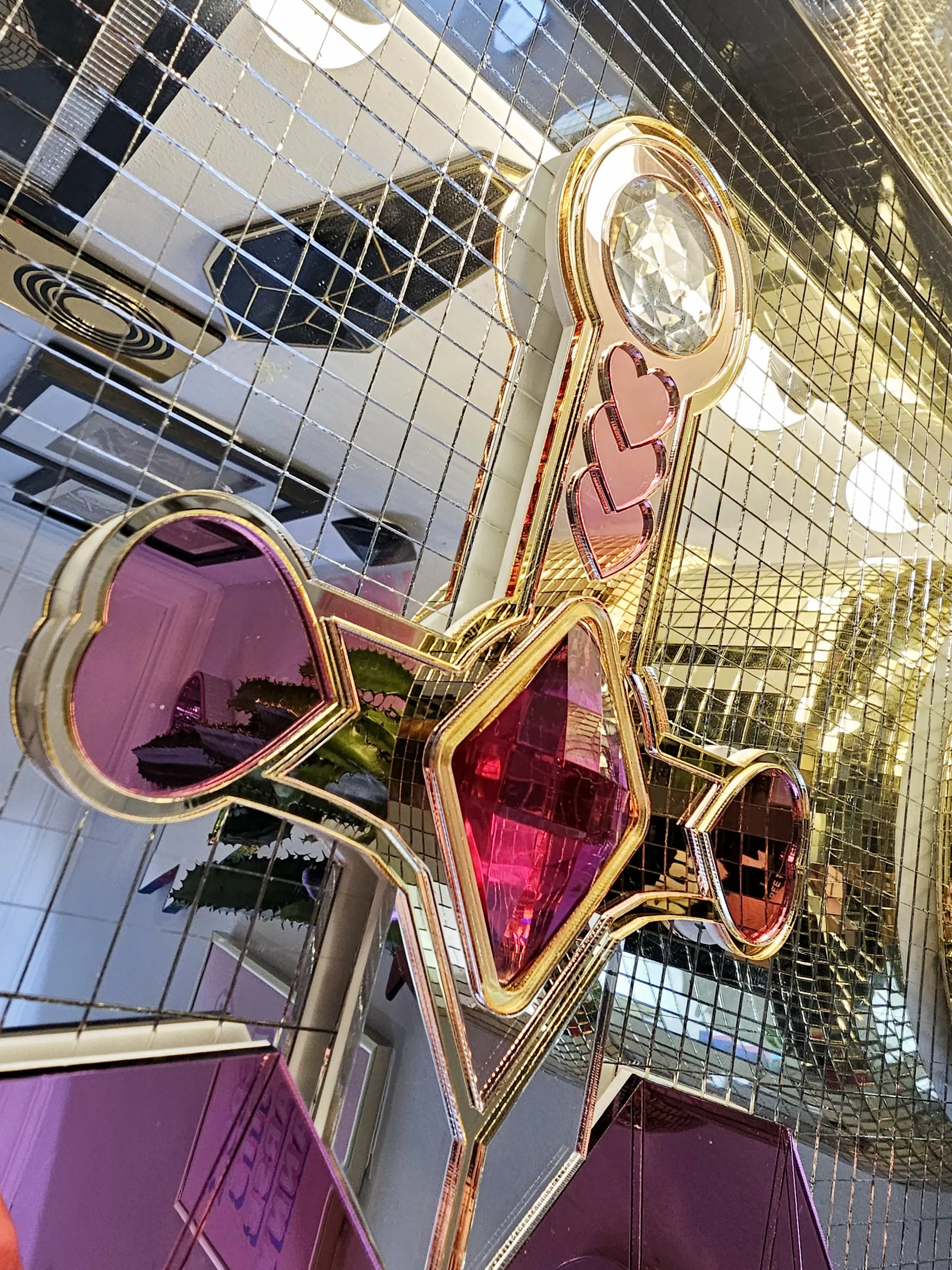 A handmade mirror on the shape of a sword piercing a heart. Made with gold, rose gold, pink and silver mirror with gem accents.