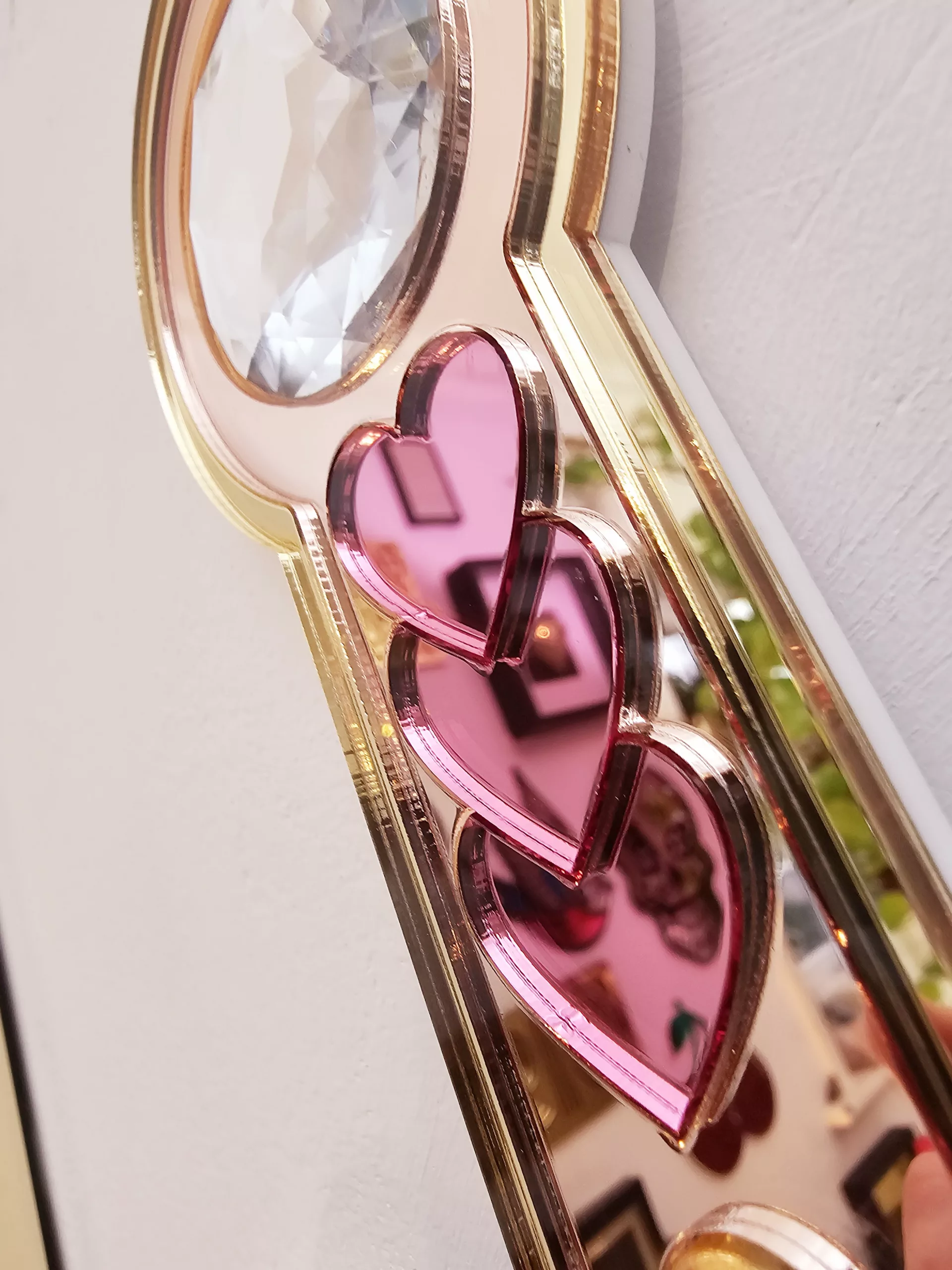 A handmade mirror on the shape of a sword piercing a heart. Made with gold, rose gold, pink and silver mirror with gem accents.