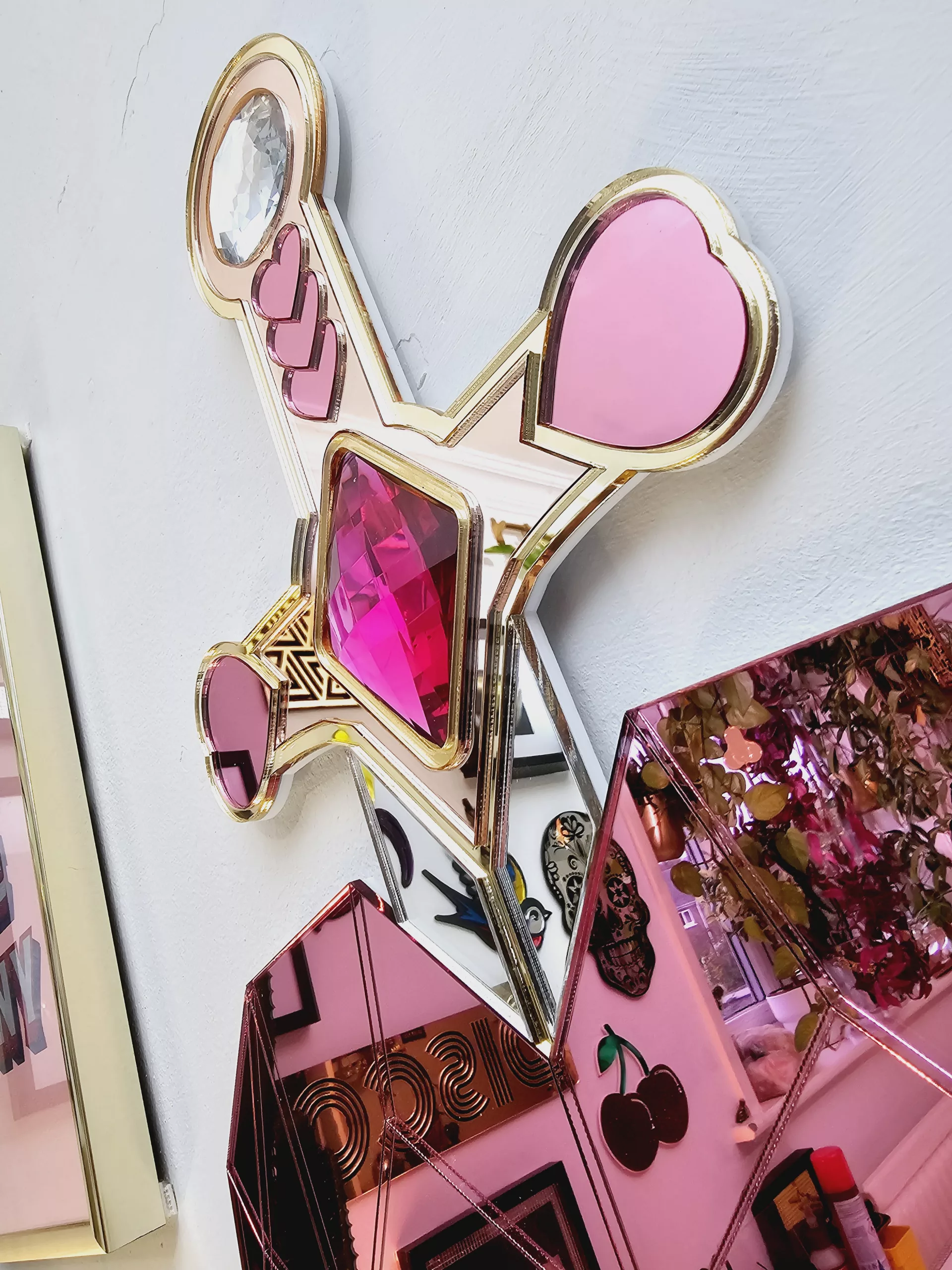 A handmade mirror on the shape of a sword piercing a heart. Made with gold, rose gold, pink and silver mirror with gem accents.